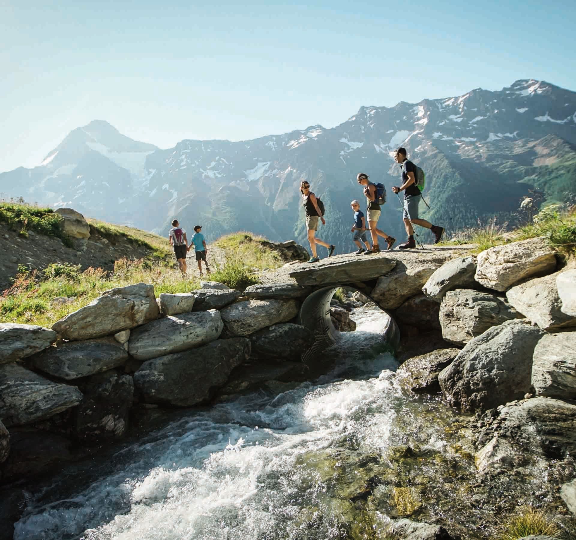 Eine Familie wandert über eine kleine Steinbrücke über einem Bach auf dem Lötschentaler Höhenweg.