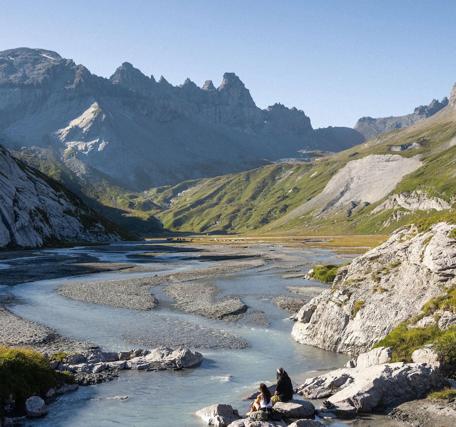 Two people sit on a stone, enjoying the expansive view of the mountain panorama and the river.