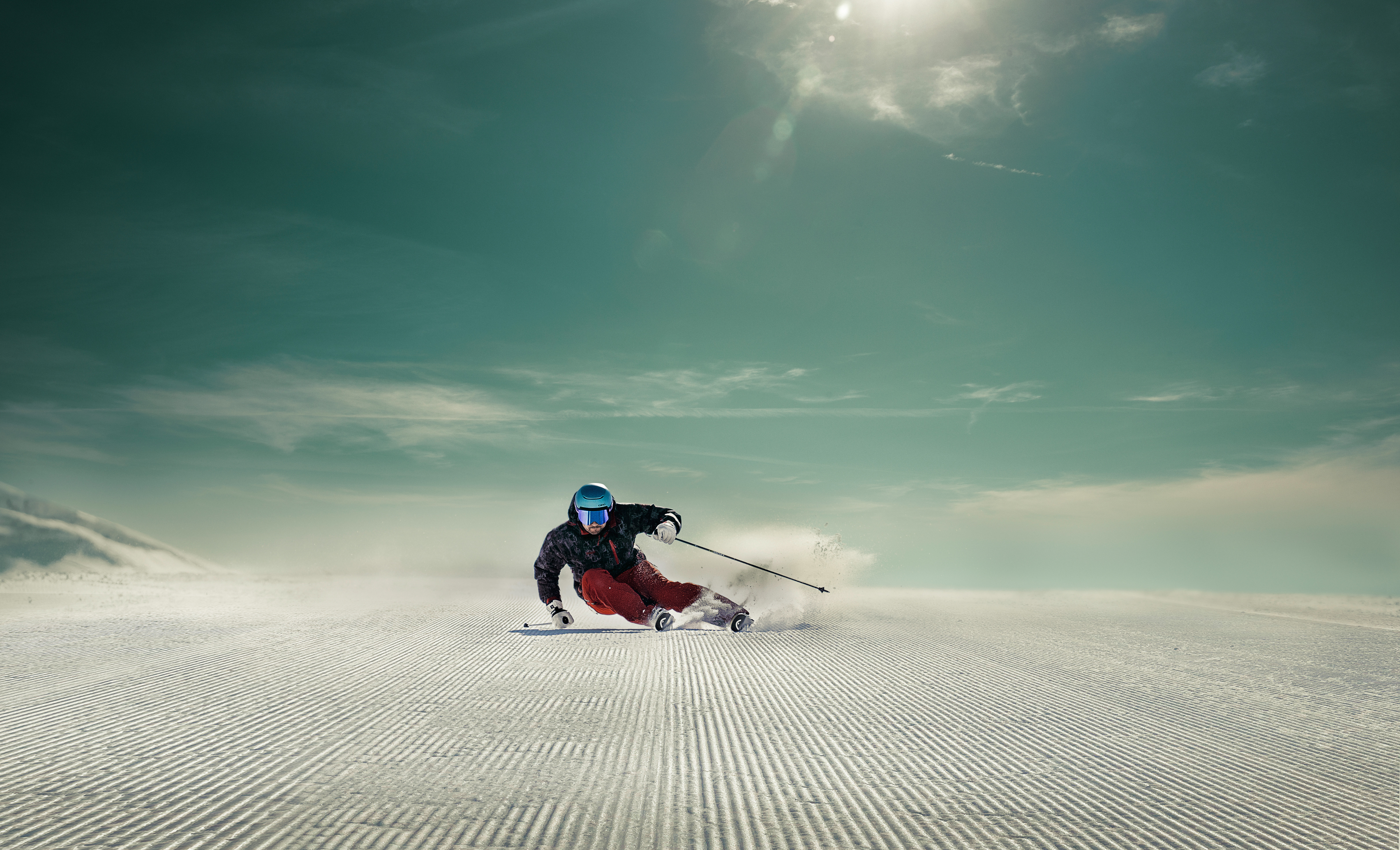 Skifahrer in roter Hose und blauem Helm fährt auf frisch präparierter Piste im Skigebiet Engelberg Titlis bei blauem Himmel.