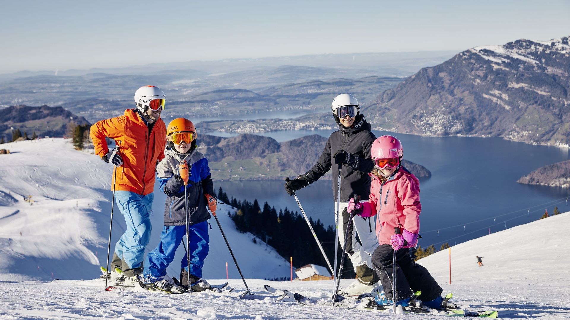 Eine Familie steht auf der Piste. Zu sehen ist das wunderschöne Berg- und Seepanorama von der Klewenalp aus.