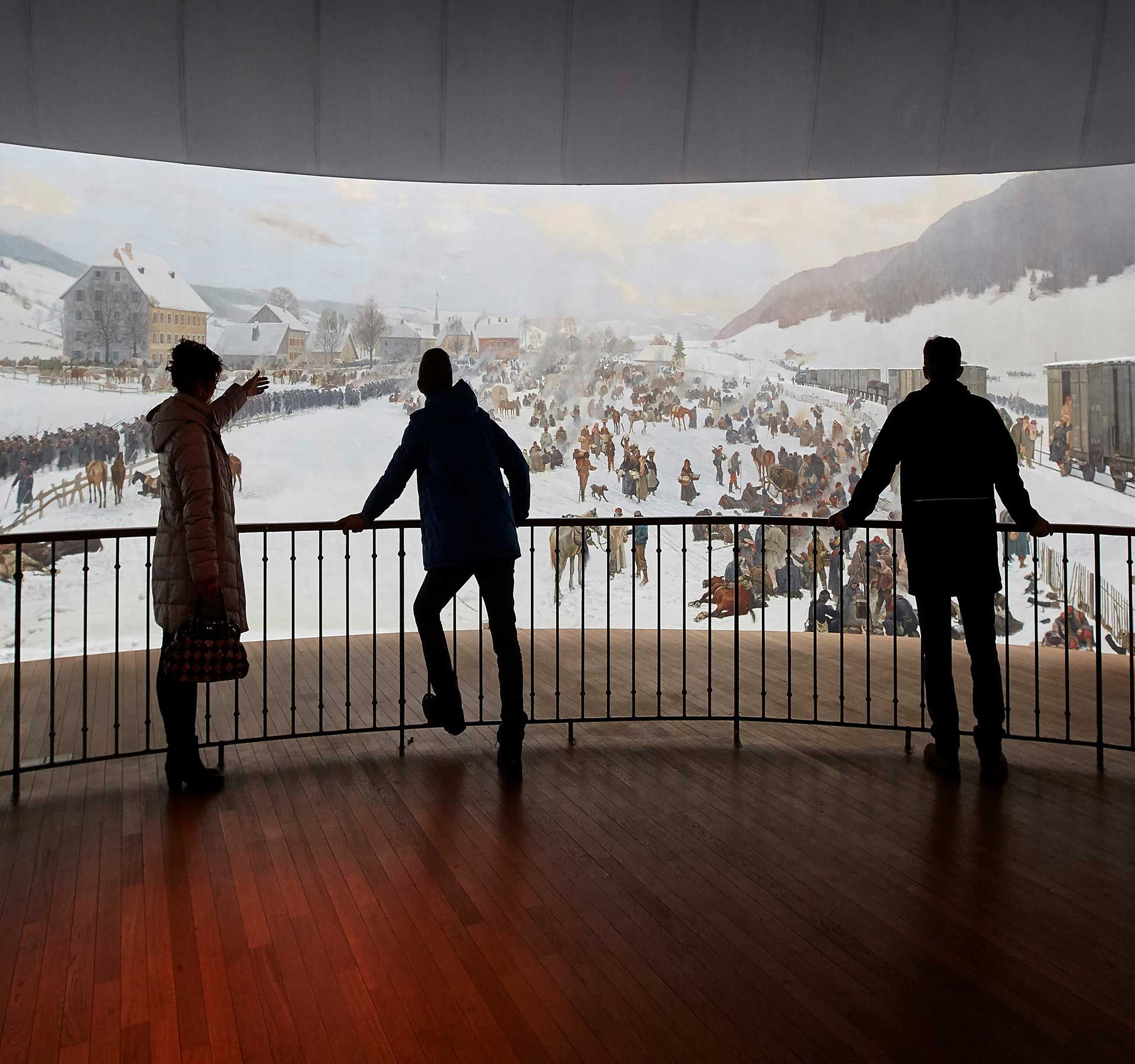 A group of people stand in front of the imposing circular painting in the Bourbaki Panorama. It shows impressions of the internment of French soldiers in Switzerland.
