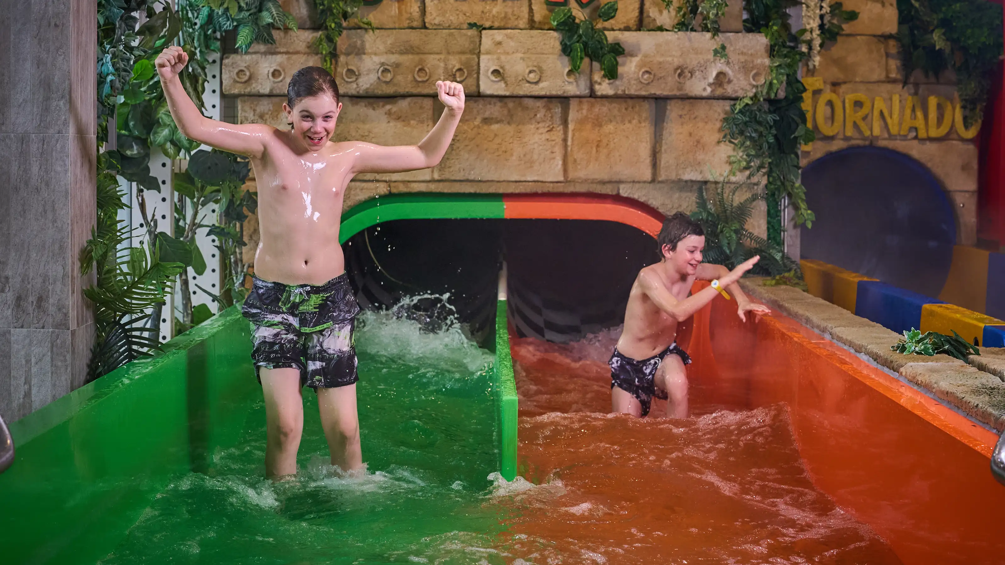 Two children stand in the water at the exit of a green and an orange water slide at Alpamare.