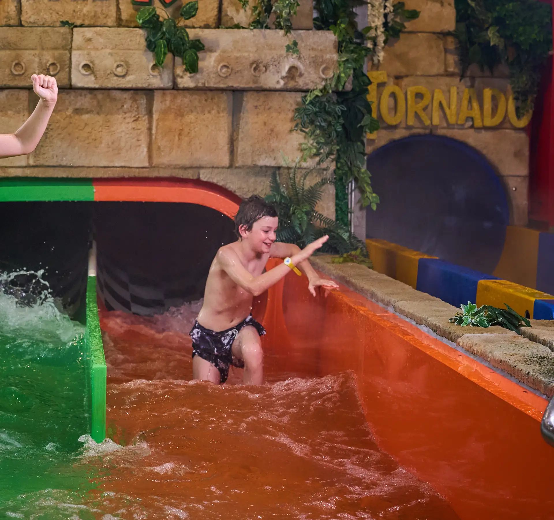 Two children stand in the water at the exit of a green and an orange water slide at Alpamare.
