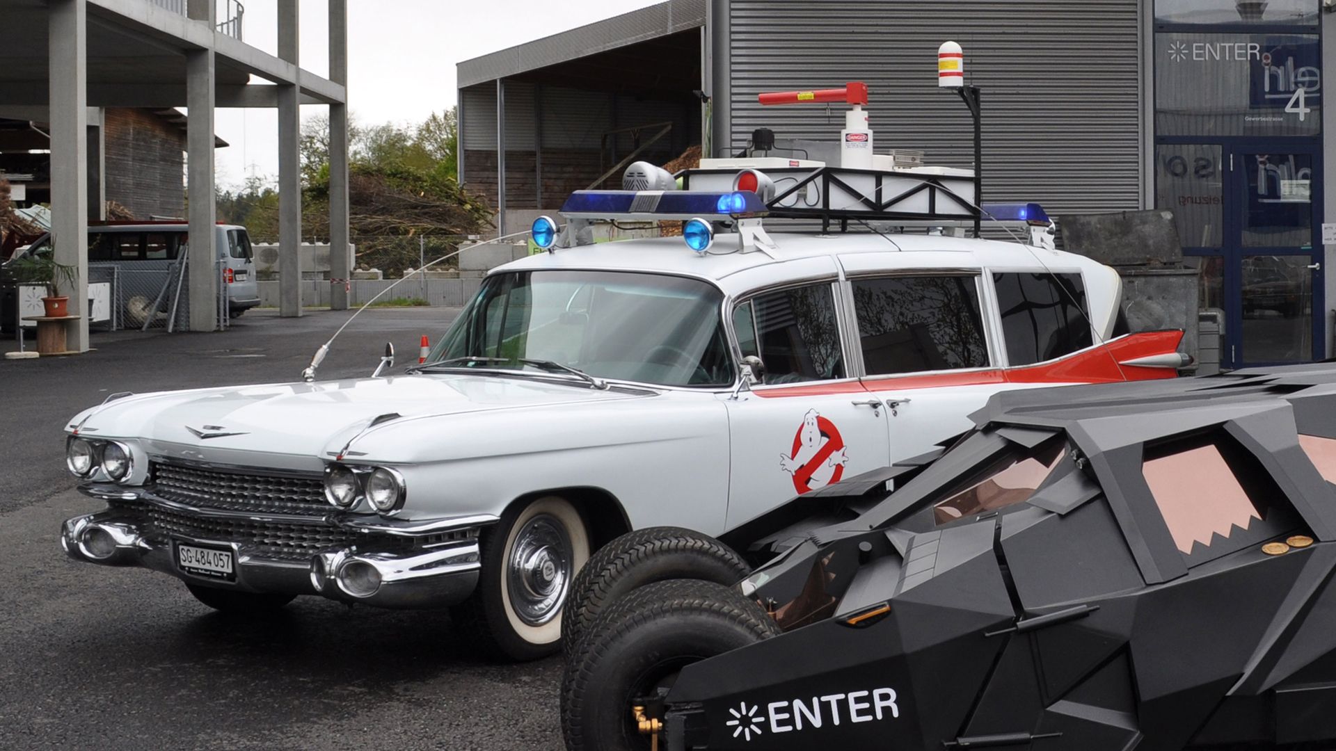 The picture shows two iconic vehicles from pop culture parked in front of a modern building with an industrial character.