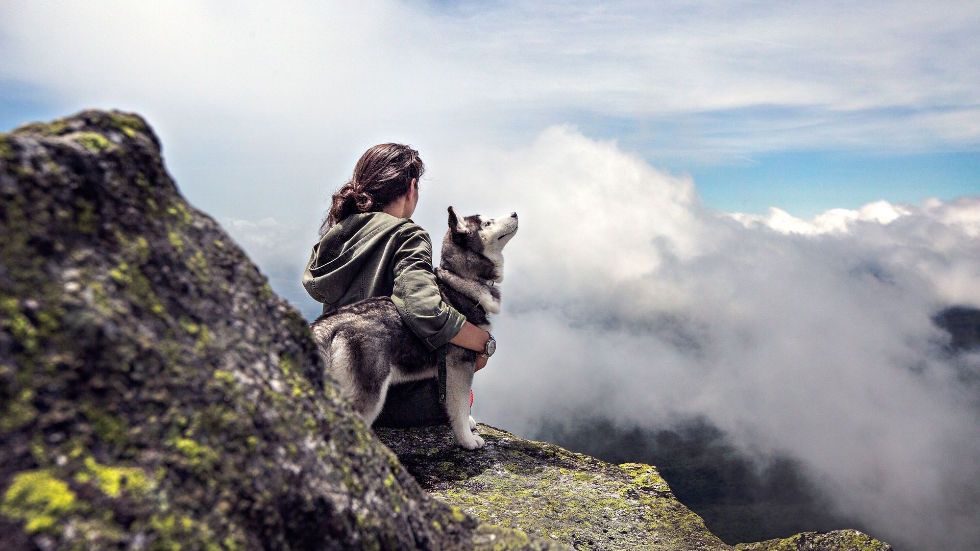 Hund und Herrchen auf einem Felsen mit Wolken