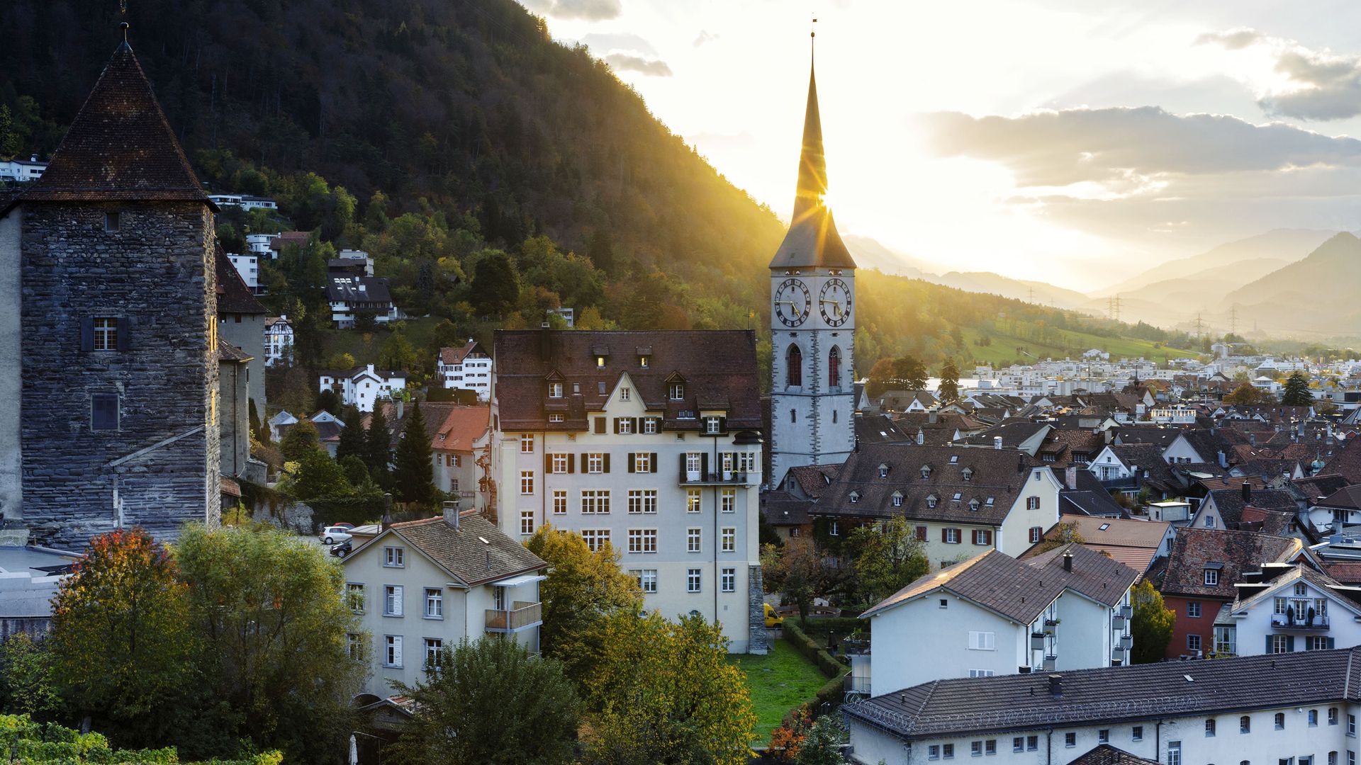 Panoramablick auf Chur in der Schweiz mit Altstadtdächern, der Martinskirche und den Bergen im Hintergrund bei Sonnenuntergang.