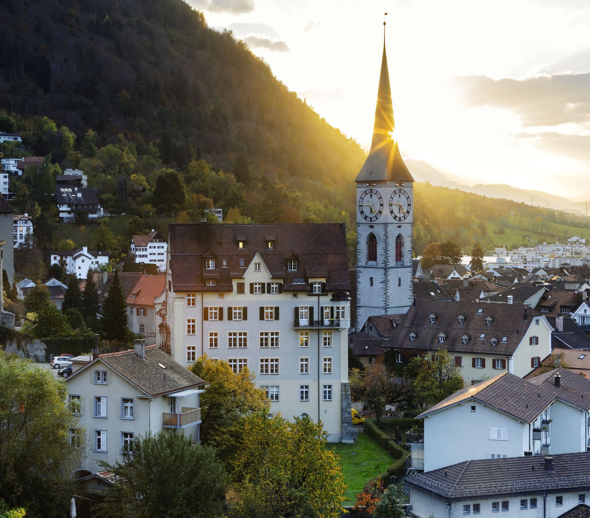 Veduta panoramica di Coira, in Svizzera, con i tetti del centro storico, la chiesa di San Martino e le montagne sullo sfondo al tramonto.