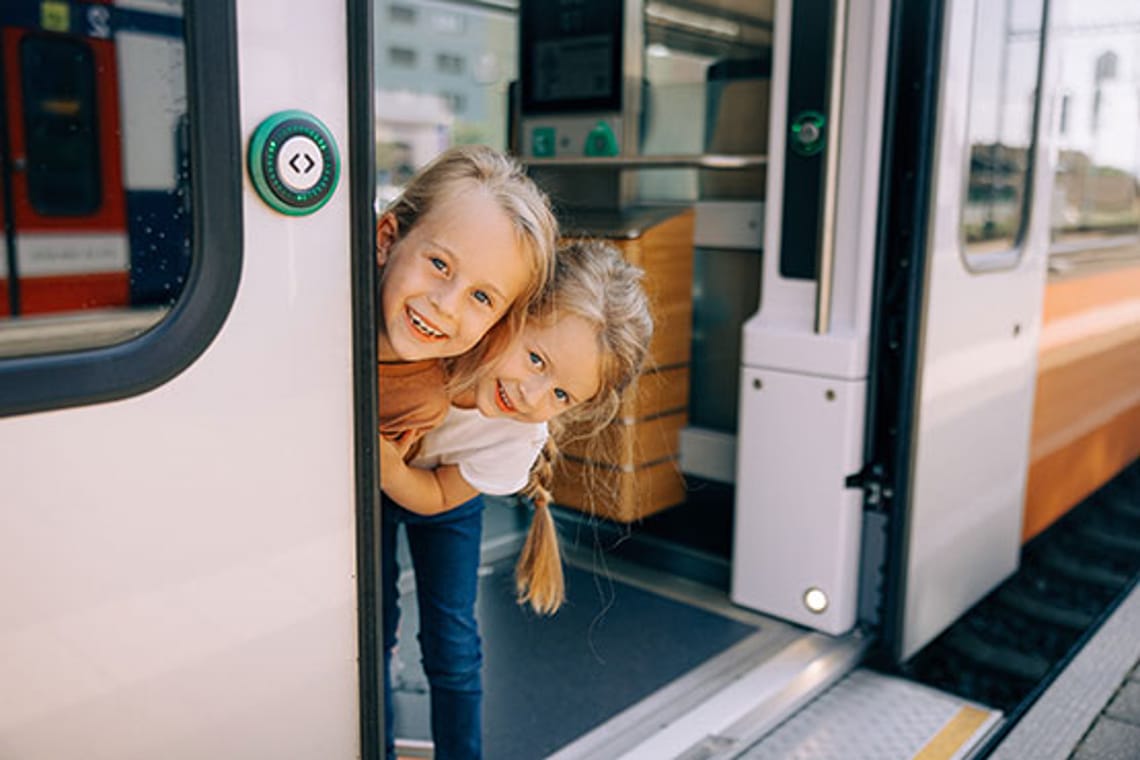 Kinder schauen fröhlich aus dem Zug, gespannt, wo die Reise hingeht.