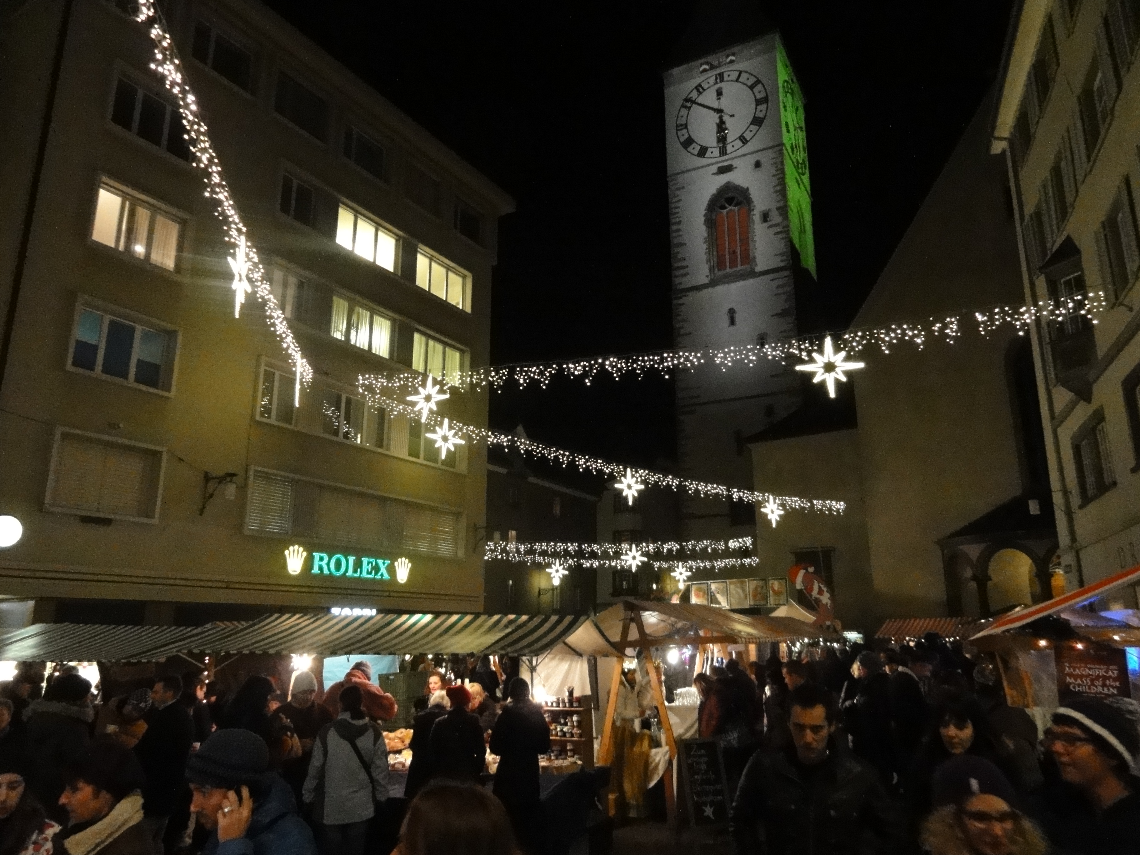 Christmas market in Chur with festive lighting, market stalls and lots of visitors in the evening.