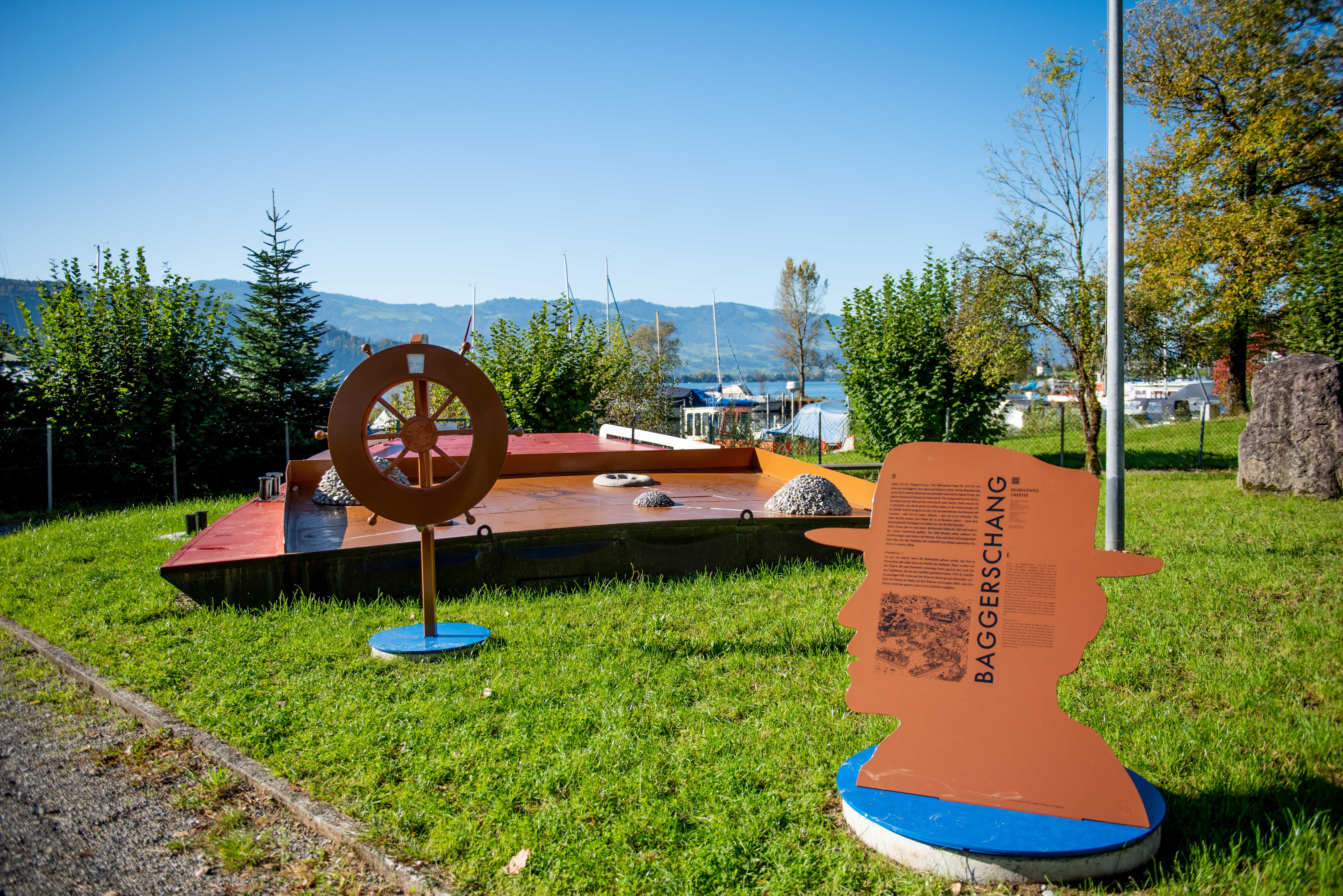 Erlebnisweg Obersee mit interaktiver Station zum Thema «Baggerschang» am Ufer des Obersees bei Rapperswil, umgeben von grüner Natur und Seehafen.