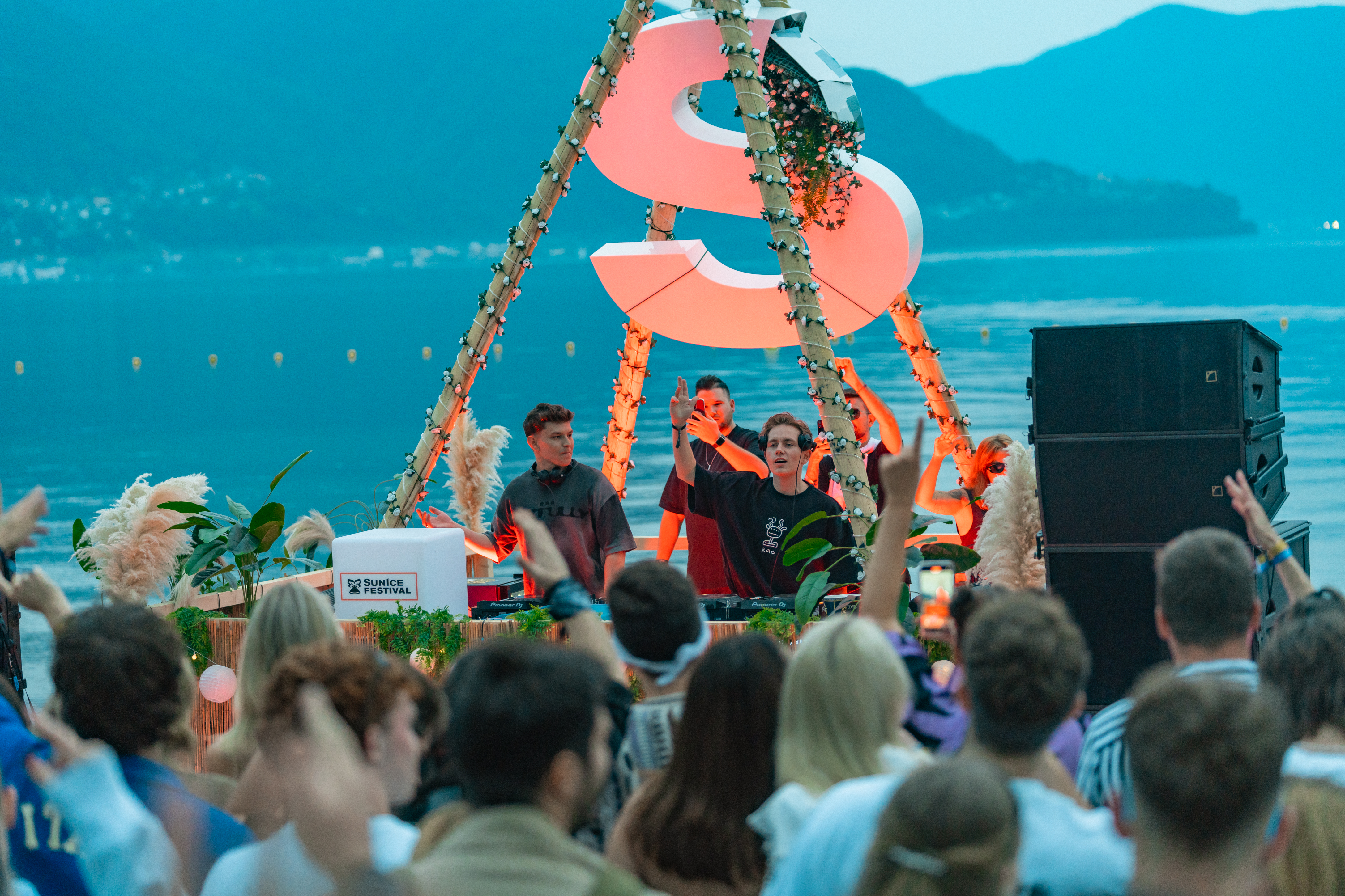 Zwei DJs vor einer Menschenmenge. Hinter ihnen ein blauer See