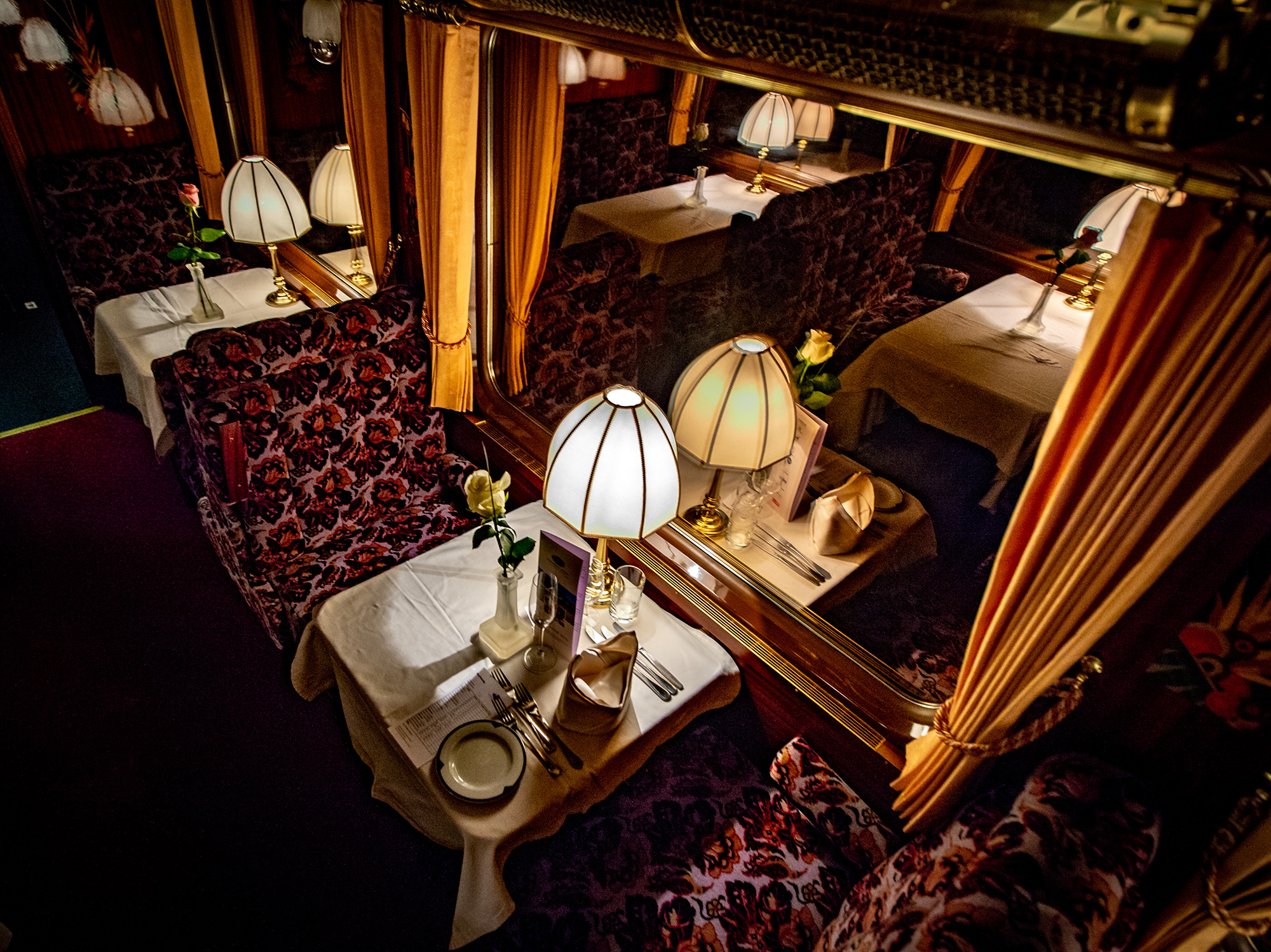 Tavolo apparecchiato nel Prestige Continental Express con lampade classiche, tovaglioli piegati e rose – atmosfera nostalgica in un vagone ristorante di lusso.