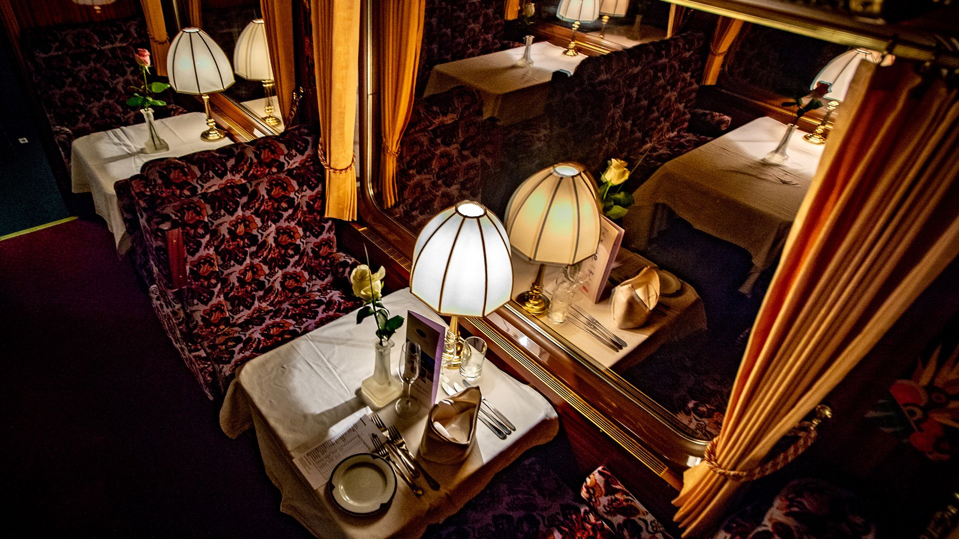 Tavolo apparecchiato nel Prestige Continental Express con lampade classiche, tovaglioli piegati e rose – atmosfera nostalgica in un vagone ristorante di lusso.