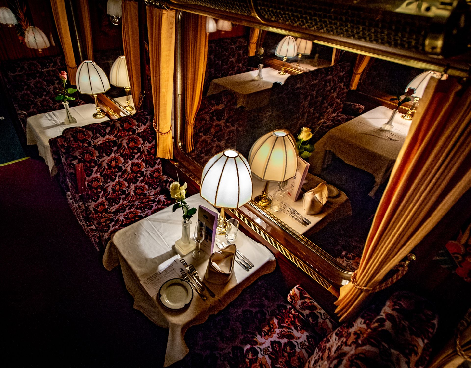 Festlich gedeckter Tisch im Prestige Continental Express mit Lampen, Stoffservietten und Rosen – nostalgische Atmosphäre im luxuriösen Speisewagen.