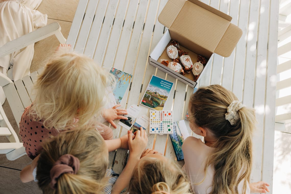 Kinder öffnen eine Überraschungsbox mit Spielen, Süssigkeiten und Broschüre