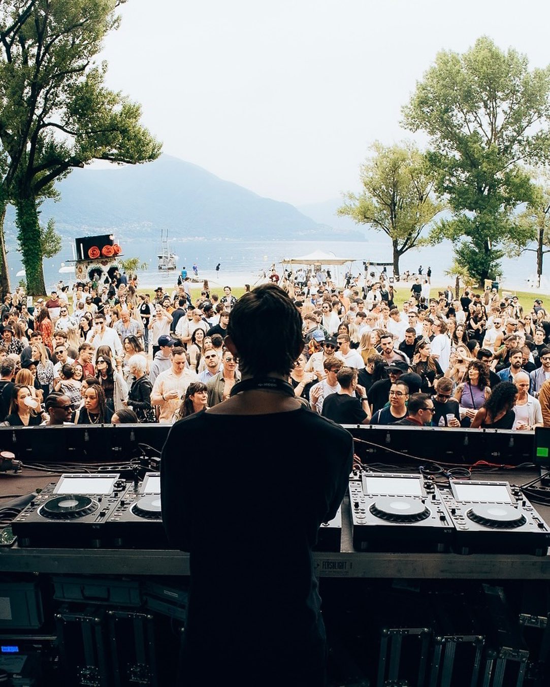A DJ in front of people. Behind them a blue lake