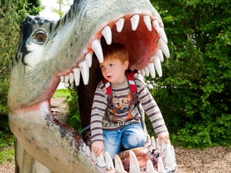 Kind spielt auf einem Spielplatz mit grosser Dinofigur
