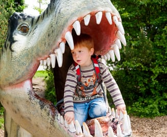 Kind spielt auf einem Spielplatz mit grosser Dinofigur