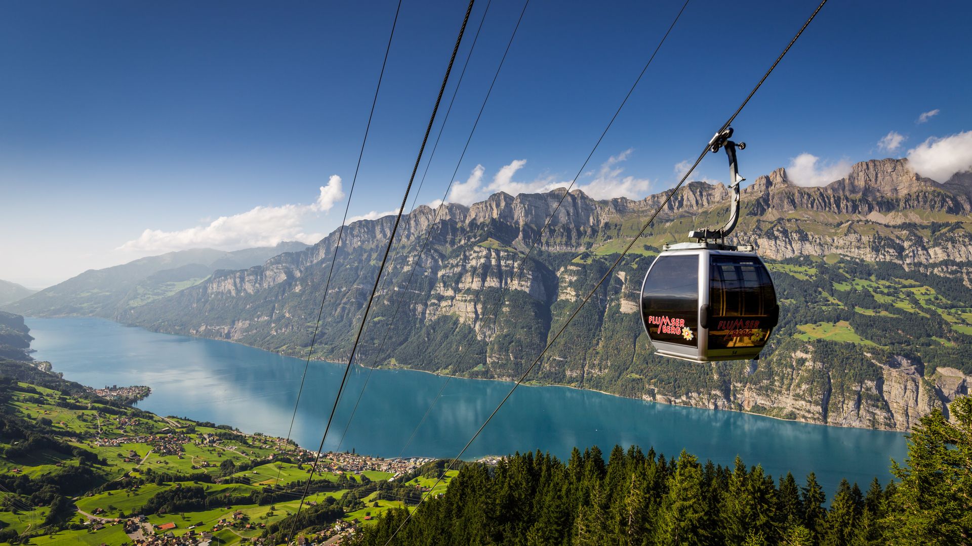 A modern SeeJet gondola gliding above the treetops at Flumserberg – with the turquoise Lake Walen, green meadows and the striking cliffs of the Churfirsten range in the background