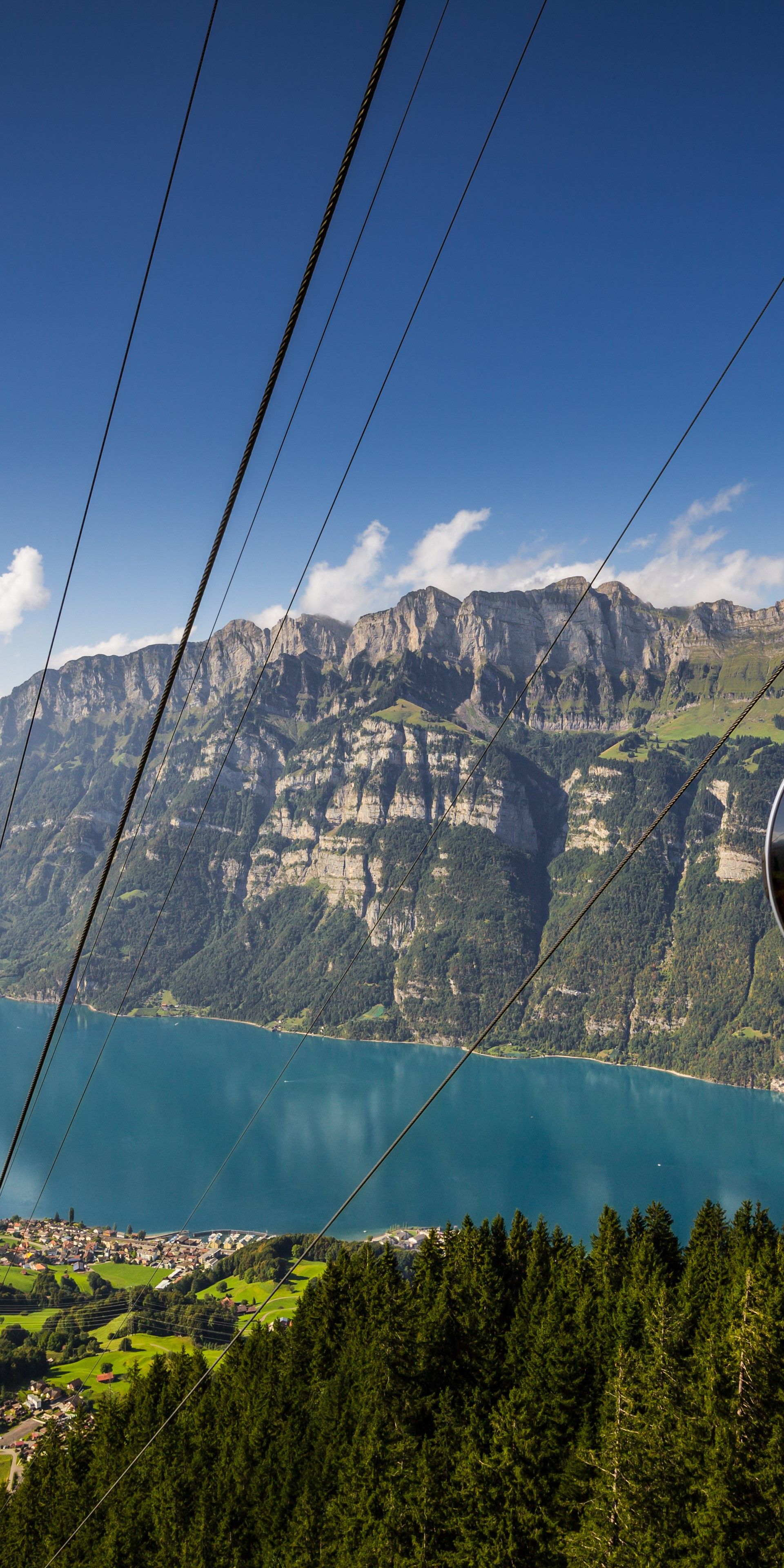 A modern SeeJet gondola gliding above the treetops at Flumserberg – with the turquoise Lake Walen, green meadows and the striking cliffs of the Churfirsten range in the background