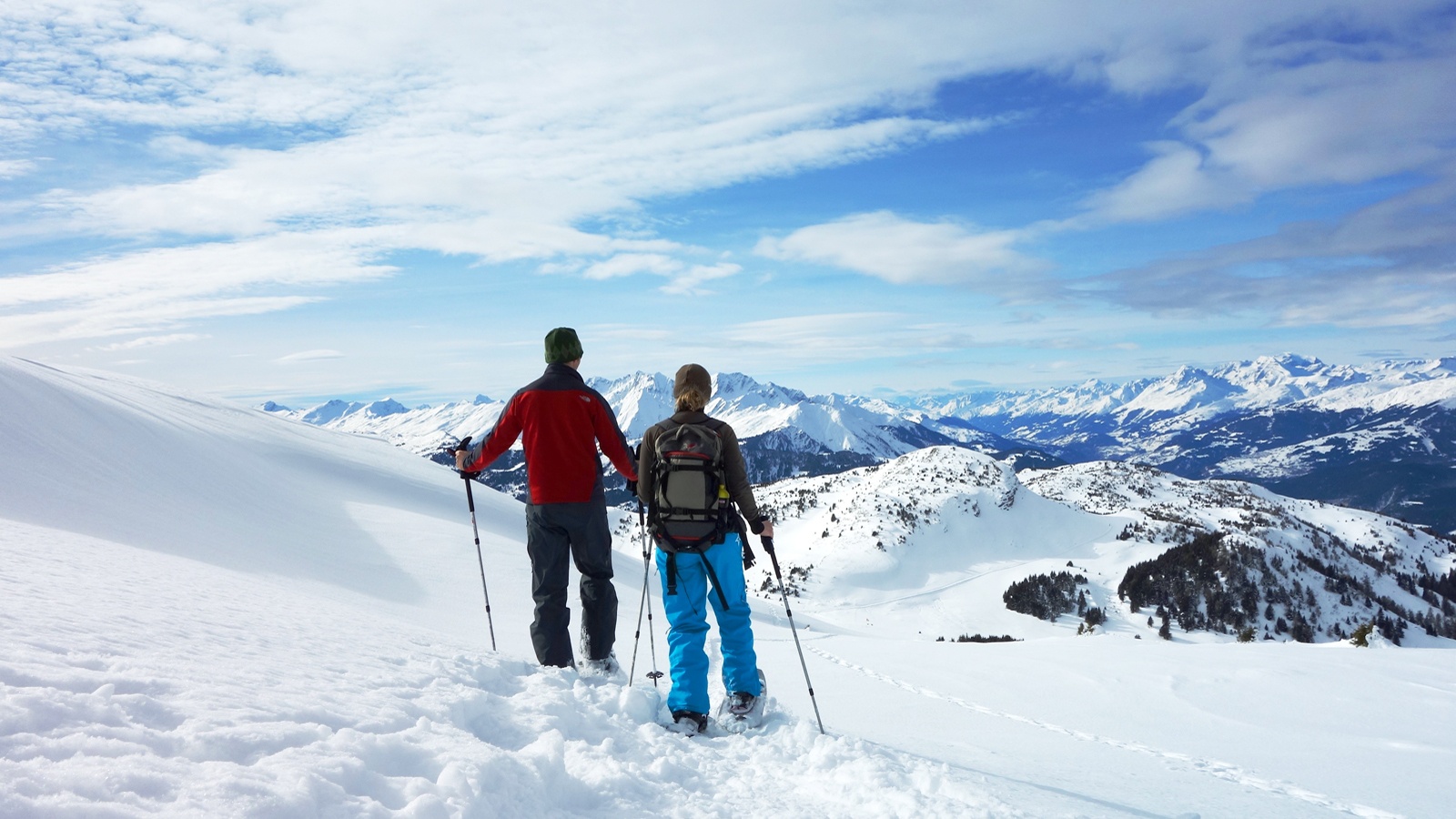 Deux personnes en randonnée hivernale sur le plateau du Dreibündenstein avec vue sur le paysage montagneux enneigé des Grisons.