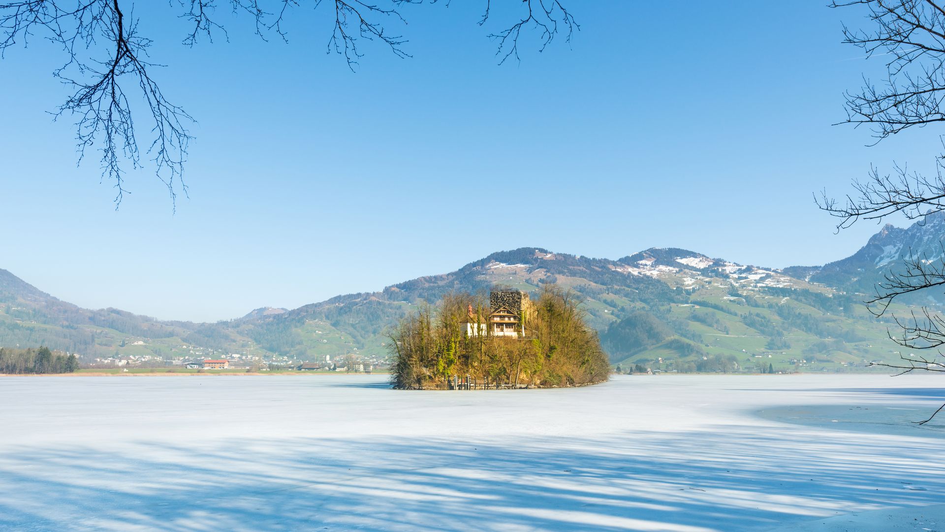 L’isola di Schwanau sul lago ghiacciato di Lauerz con montagne innevate e cielo azzurro limpido.