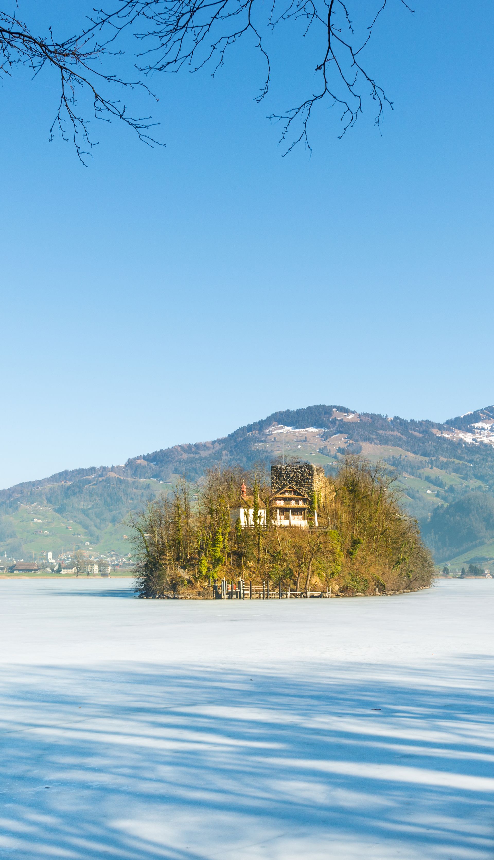 L’isola di Schwanau sul lago ghiacciato di Lauerz con montagne innevate e cielo azzurro limpido.