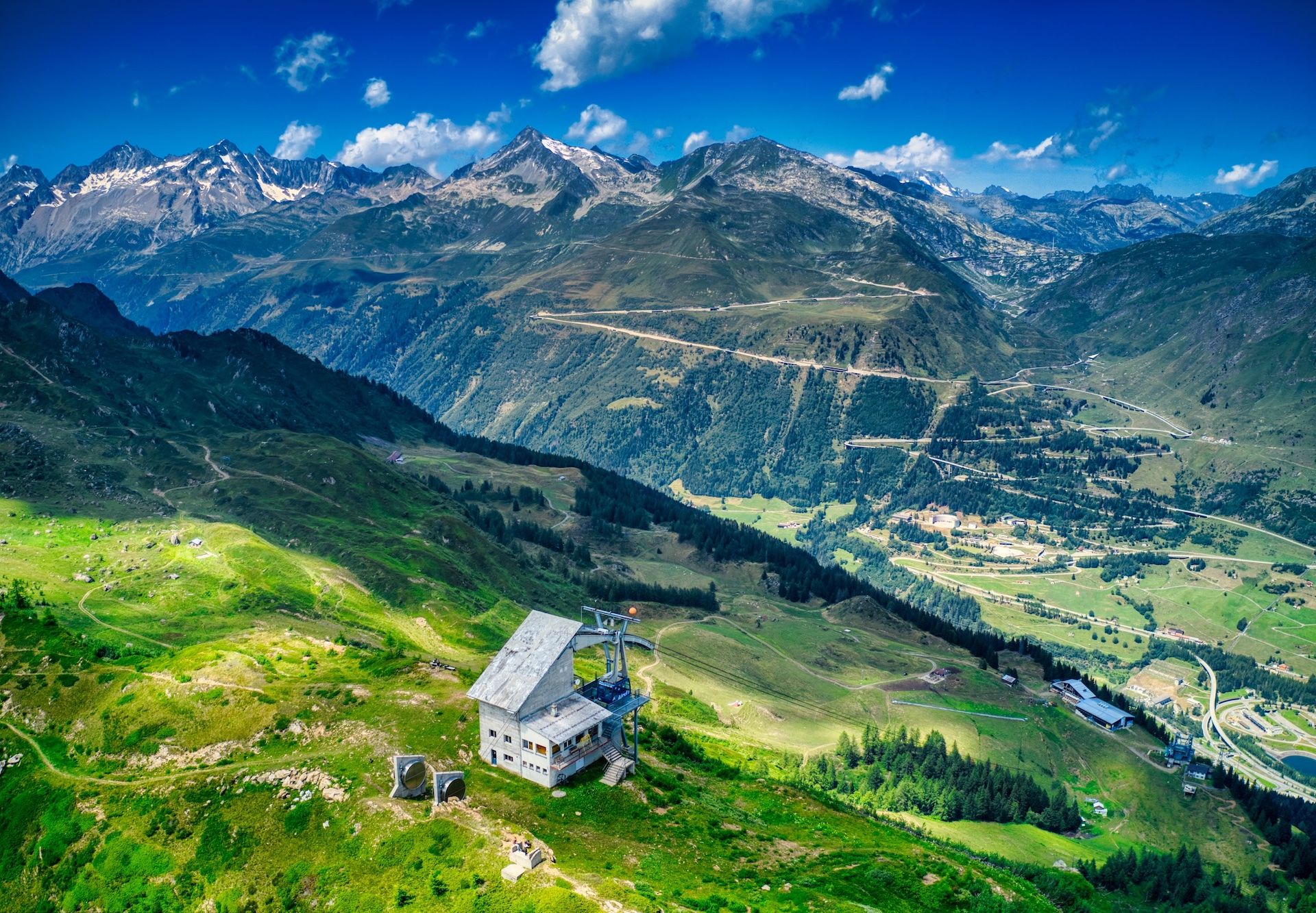 Wooden bench along the Strada degli Alpi in the Bedretto Valley, with panoramic views of the Ticino Alps and snow-covered peaks.