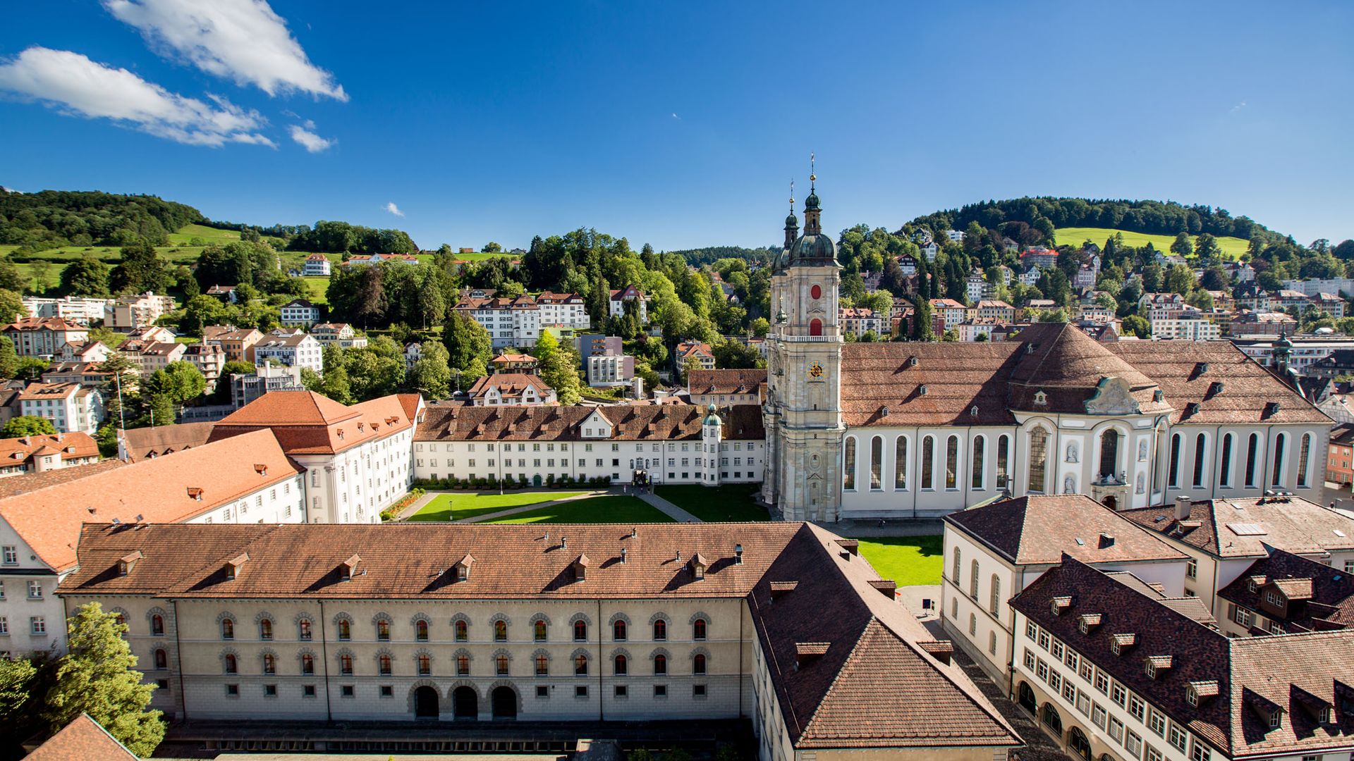 The Abbey District of St. Gallen with its baroque cathedral and monastery buildings, surrounded by the old town and green hills.