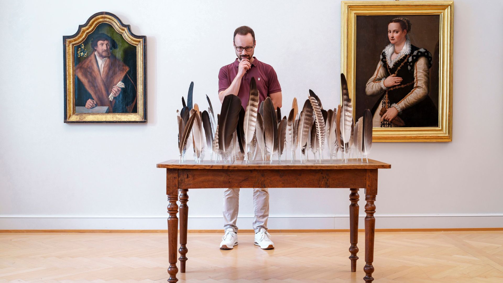Visiteur observant une installation artistique moderne composée de plumes au musée d’art de Saint-Gall, entouré de portraits classiques.
