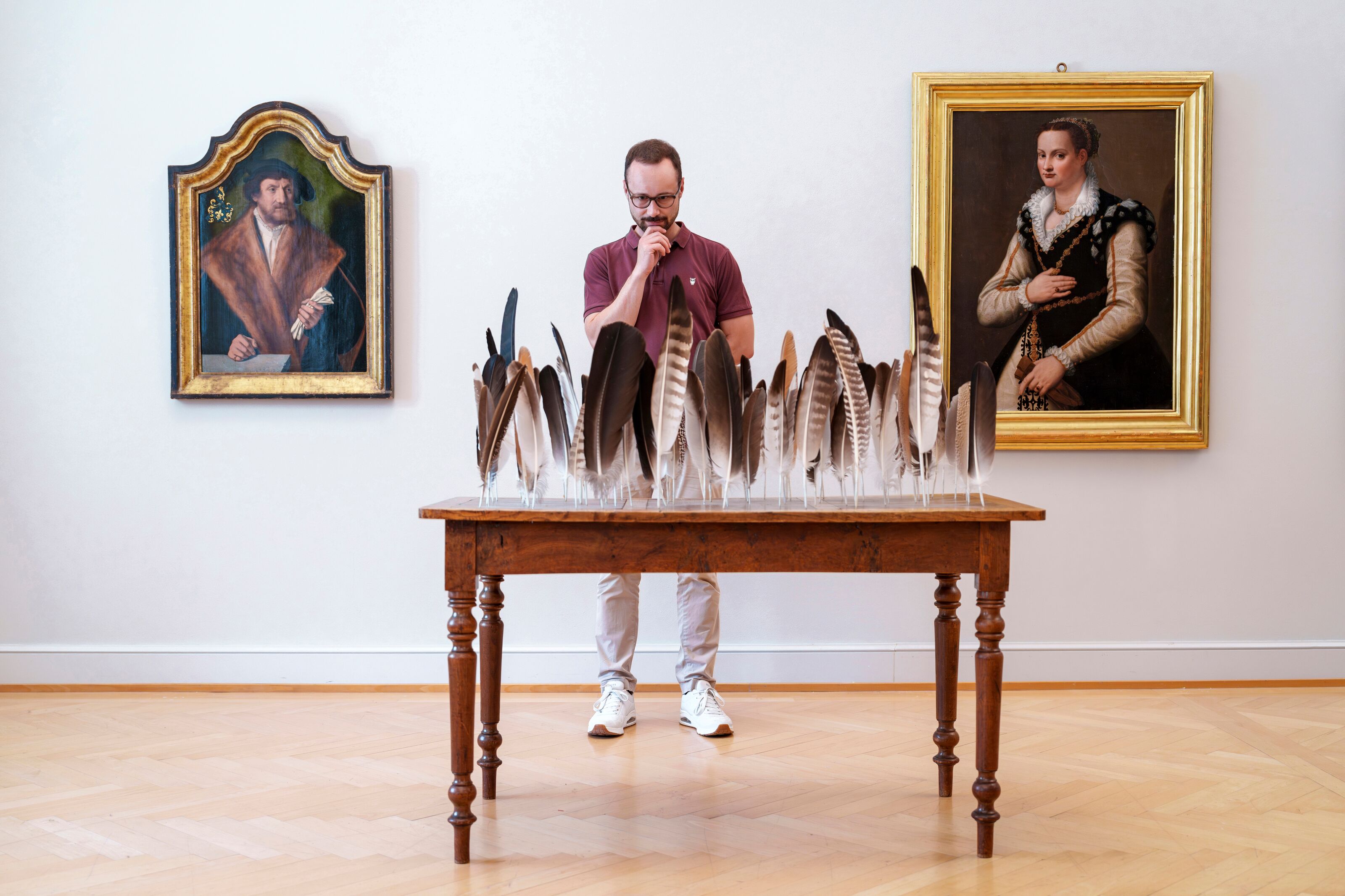 Ein Tisch mit Federn, dahinter ein Mann, welcher das Kunstwerk im Kunstmuseum St.Gallen betrachtet