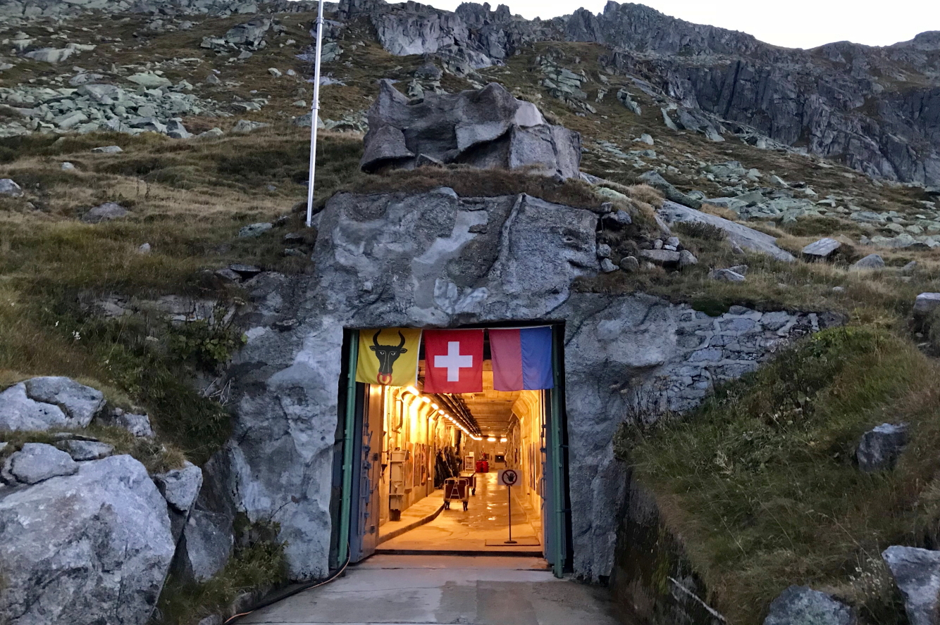 Eingang der Gotthardfestung Sasso San Gottardo – in den Fels eingelassener Zugang mit Schweizer Flagge und Tunnelbeleuchtung auf dem Gotthardpass.