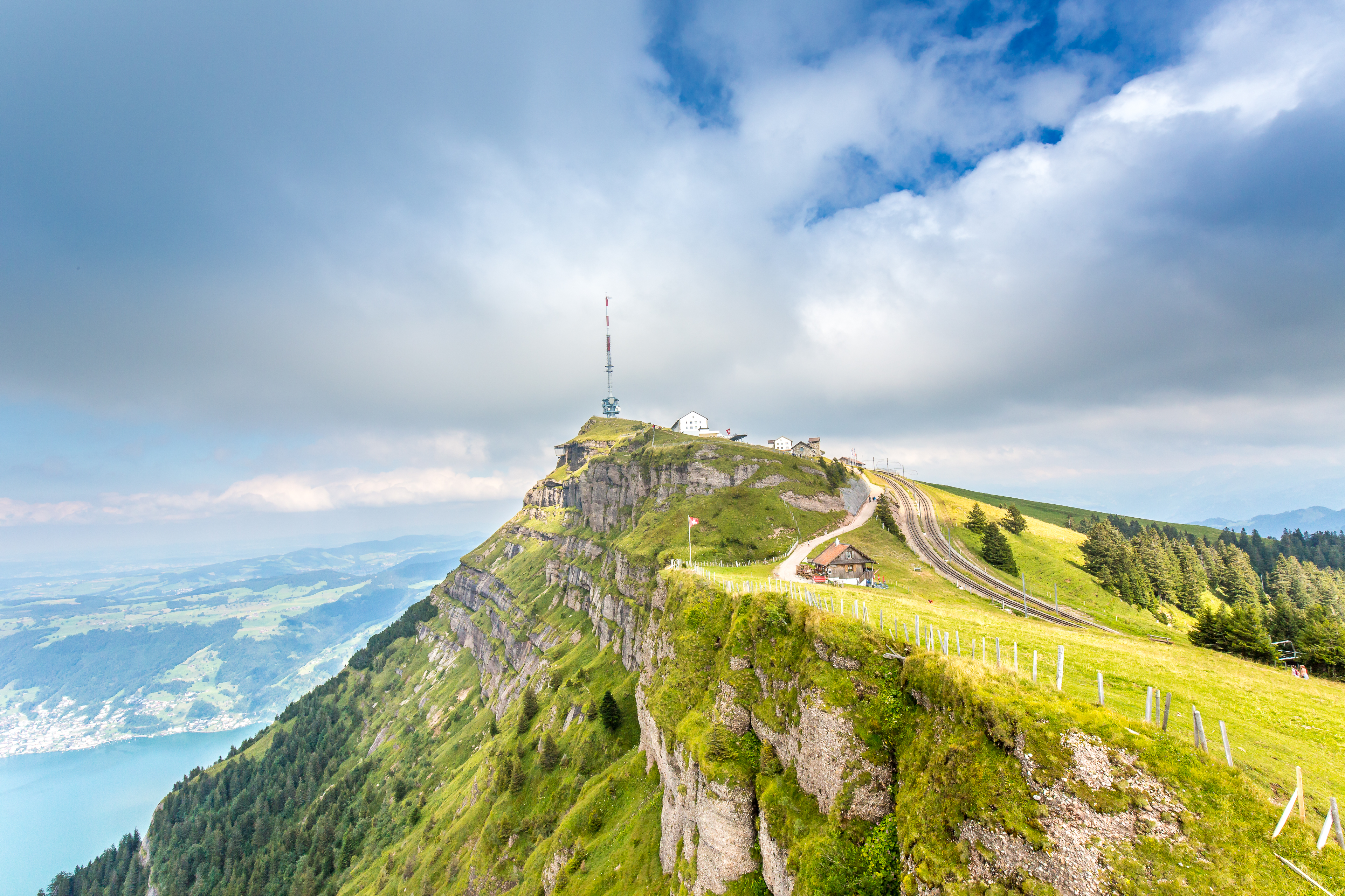 Blick auf den Gipfel der Rigi Kulm mit Bergstation, Sendeturm und Bahntrasse, im Hintergrund der Vierwaldstättersee und die Zentralschweiz.
