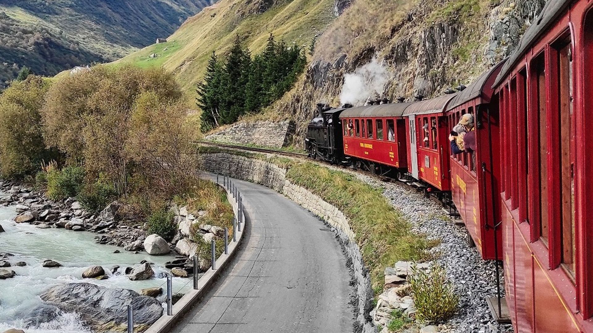 Die Dampfbahn Furka-Bergstrecke schlängelt sich mit historischen roten Wagen entlang der Reuss – eine eindrucksvolle Fahrt durch die alpine Landschaft zwischen Realp und Oberwald.
