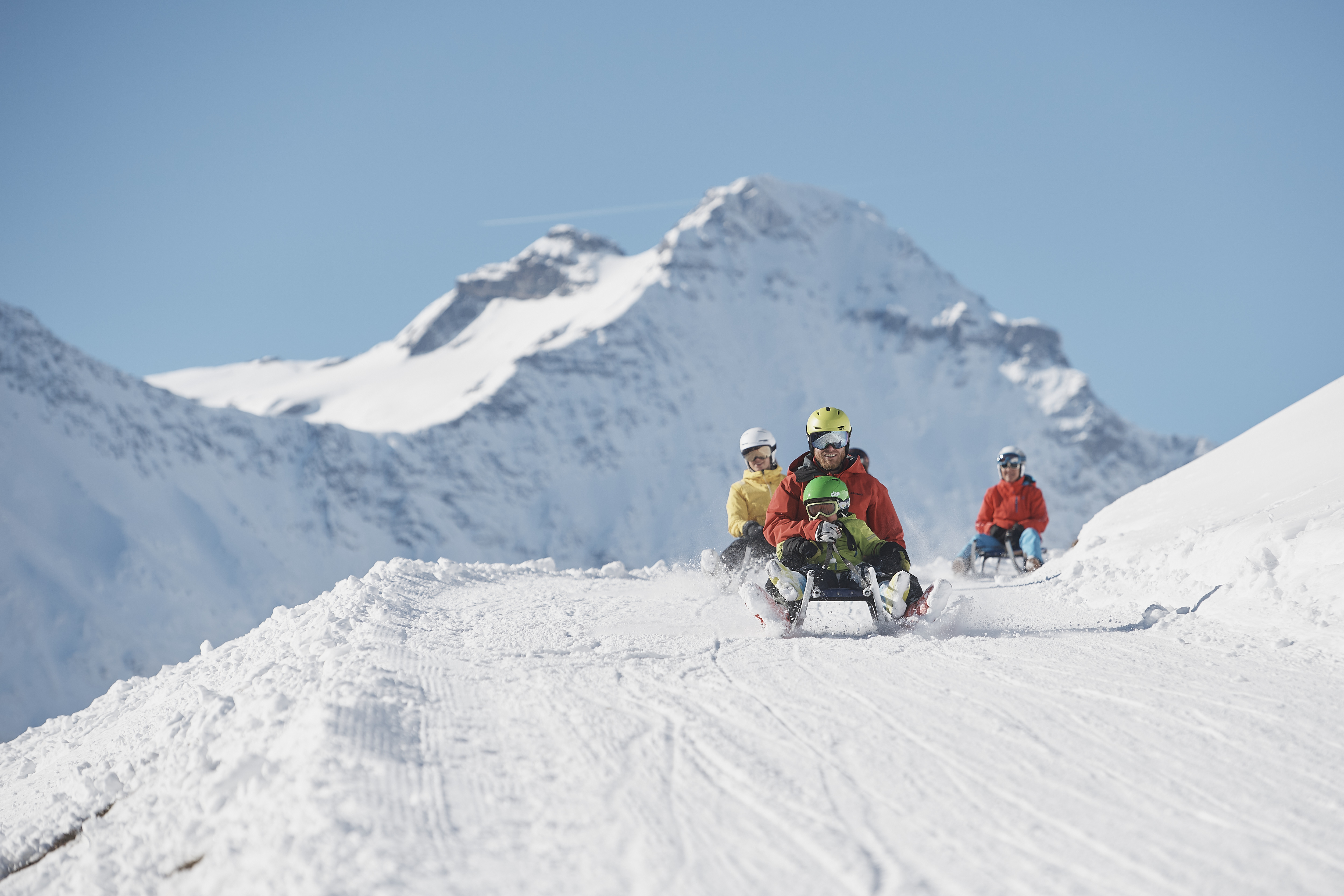 Trois personnes et un enfant faisant de la luge devant un panorama de montagne à Elm