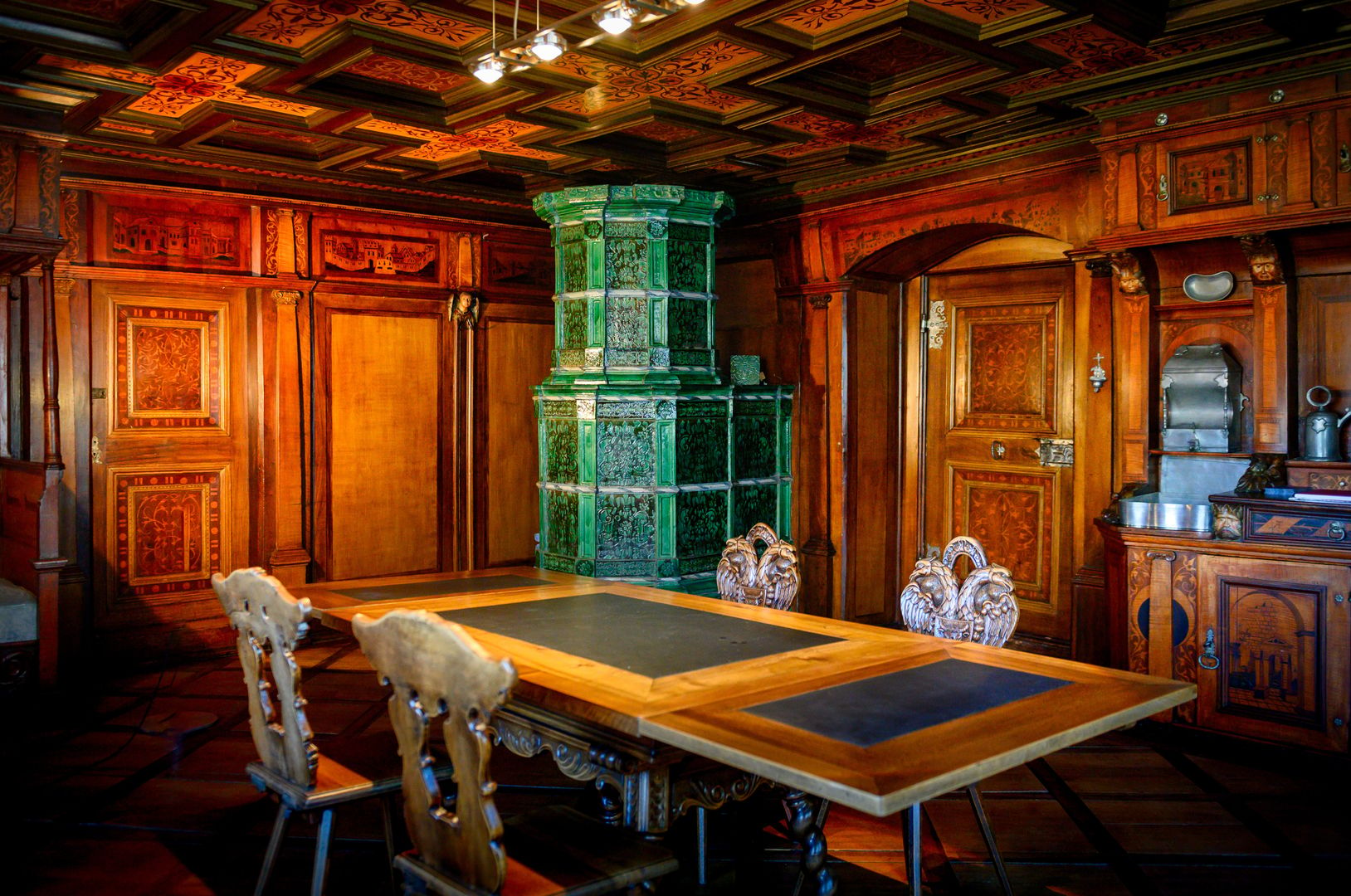 Zimmer aus Holz mit grünem Kamin, Tisch um den 4 Stühle stehen