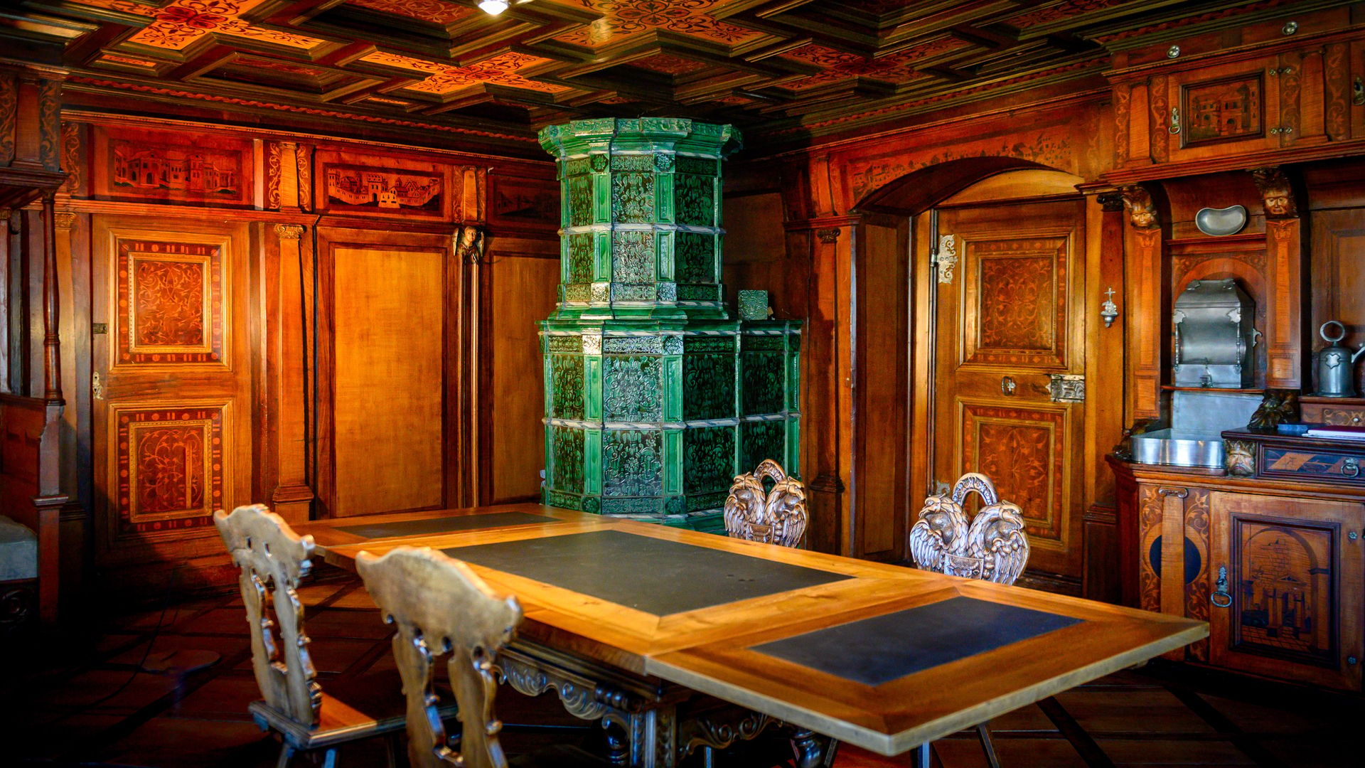 Zimmer aus Holz mit grünem Kamin, Tisch um den 4 Stühle stehen