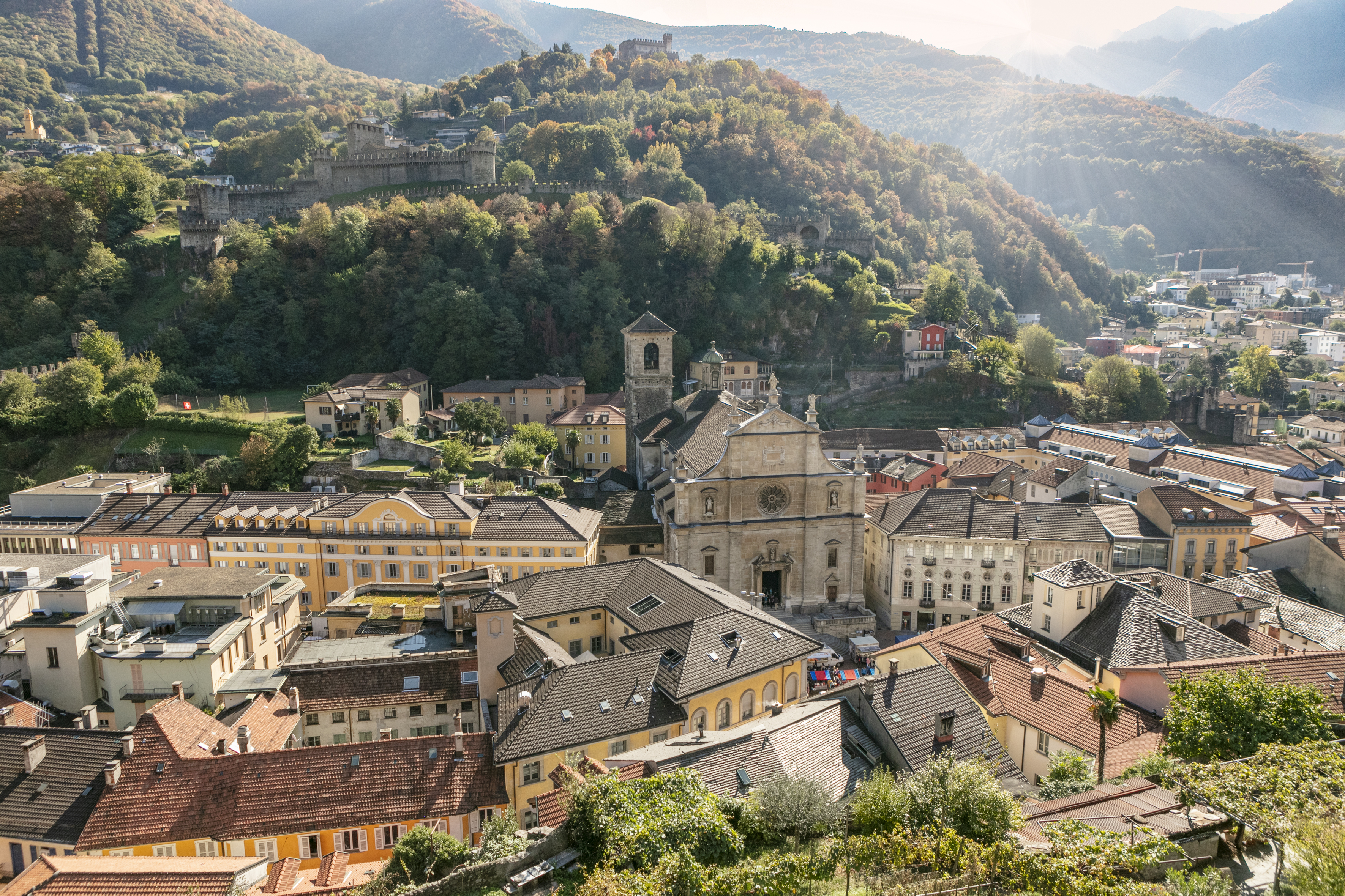 Vue sur la vieille ville de Bellinzona avec l’église San Biagio et les châteaux médiévaux, entourée de collines aux couleurs automnales dans le canton du Tessin.