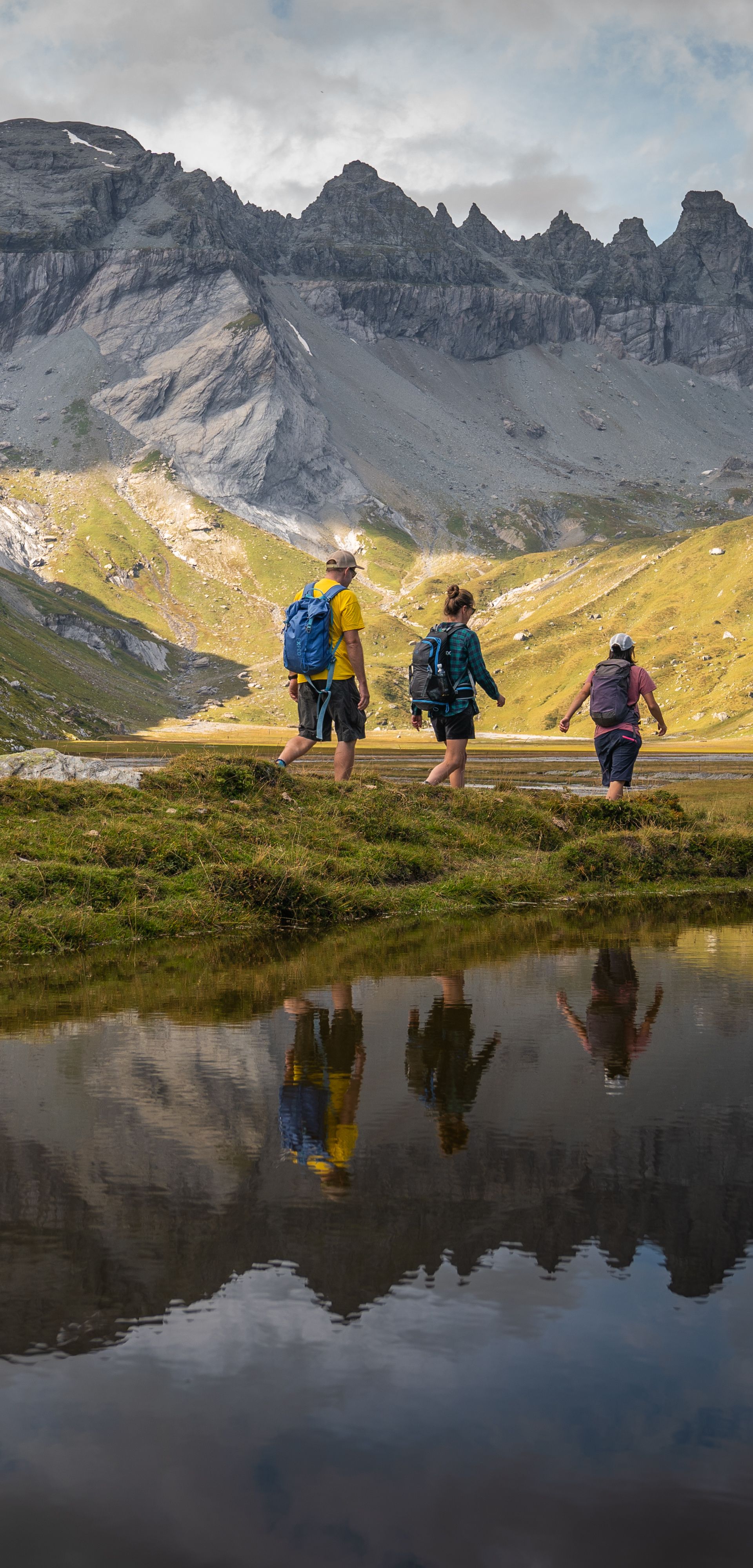 Escursionisti sull’altopiano di Segnes sopra Flims, nell’Arena tettonica di Sardona, circondati da pareti rocciose grigie e pascoli alpini verdi, con il riflesso delle montagne nell’acqua – paesaggio suggestivo dei Grigioni.