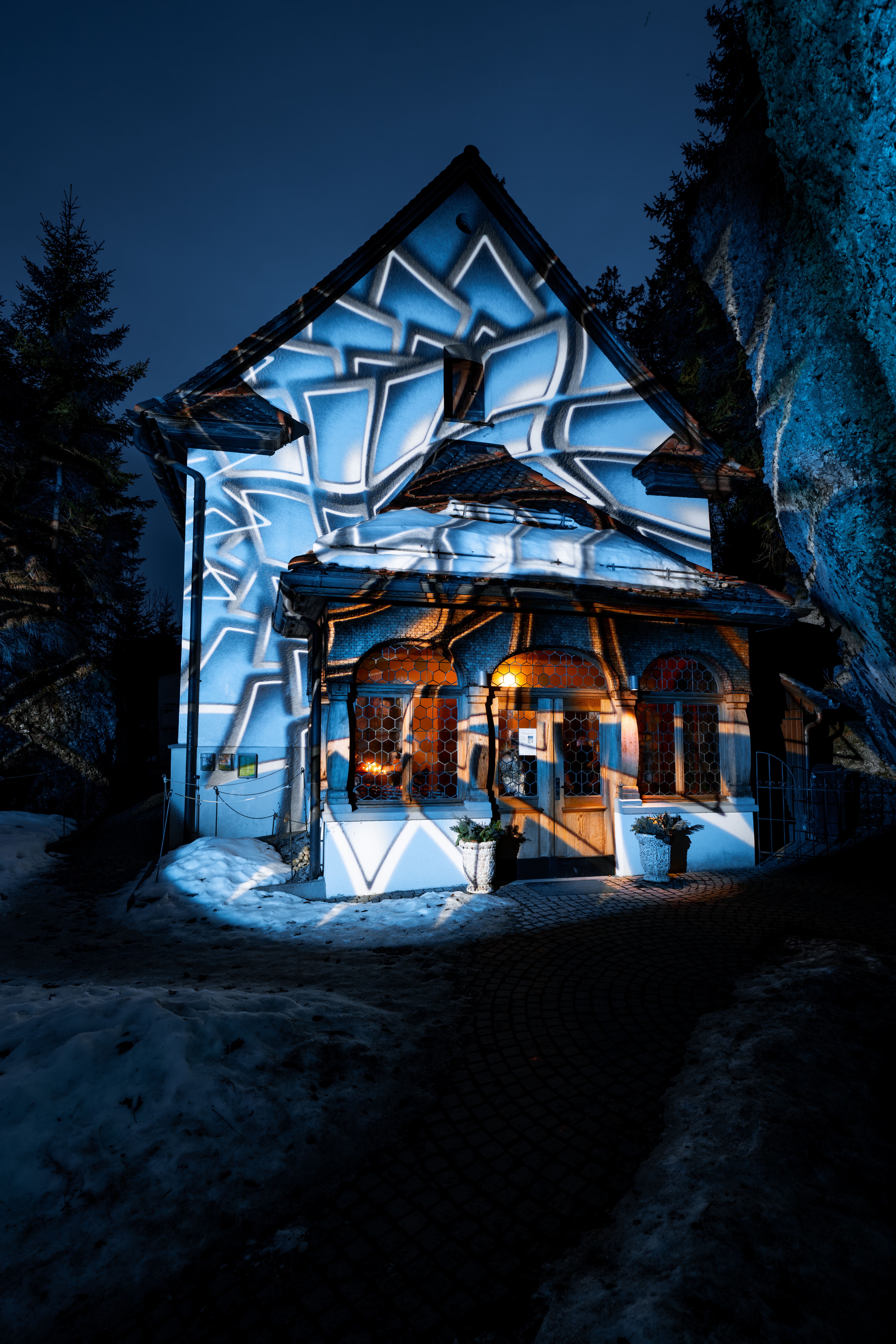 Historisches Gebäude auf der Rigi mit kunstvoller Lichtprojektion an der Fassade, umgeben von Schnee und Felsen in der Nacht.