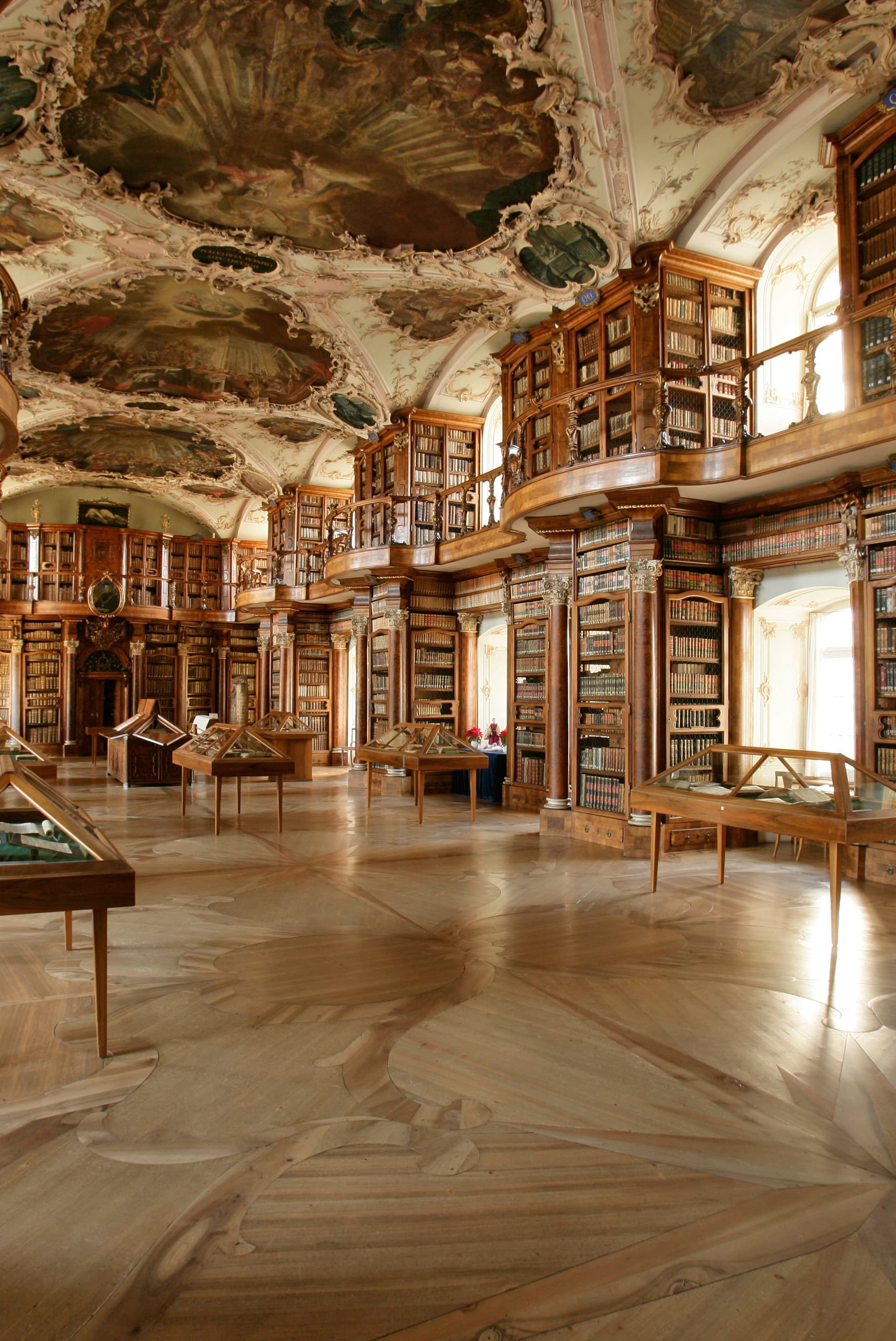 The baroque library hall of the Abbey Library of St. Gallen with ornate ceiling paintings and historic bookshelves.