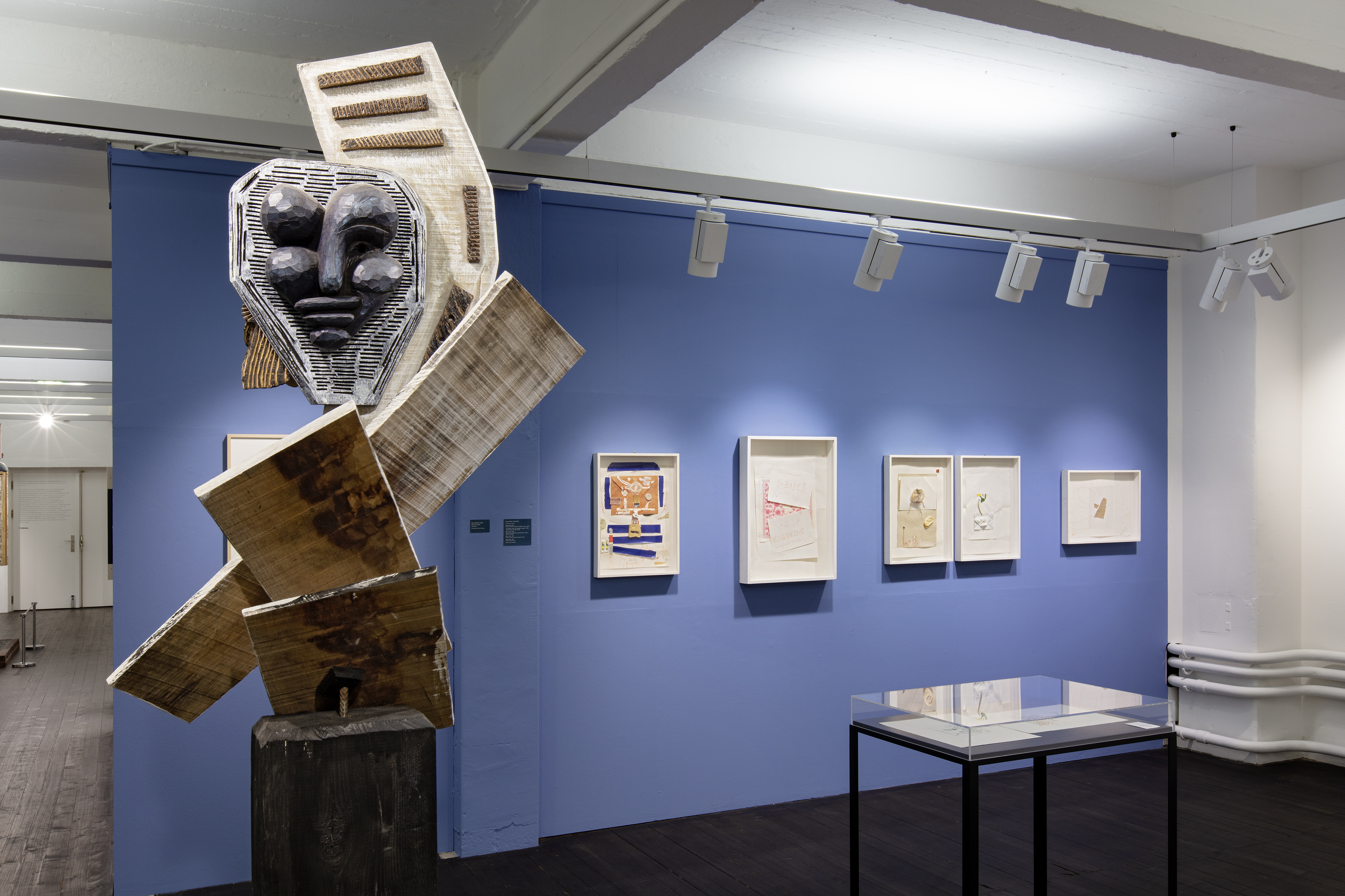 Innenansicht der Museumsräume. Im Vordergrund steht eine Skulptur mit Gesicht aus Holz. Im Hintergrund hat es eine blaue Wand mit Kunstwerken.