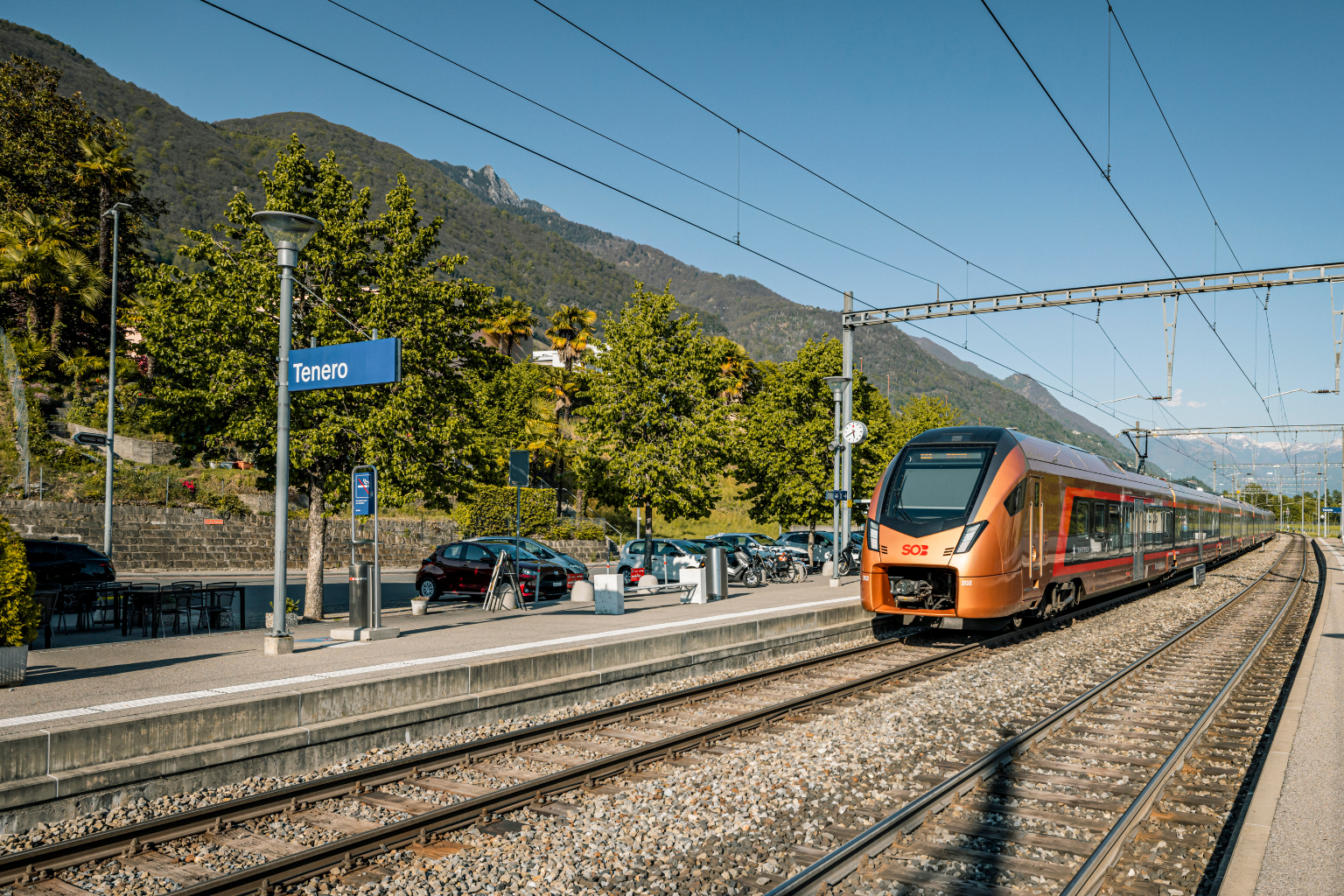 Kupferfarbener Zug hält am Bahnhof in Tenero, TI