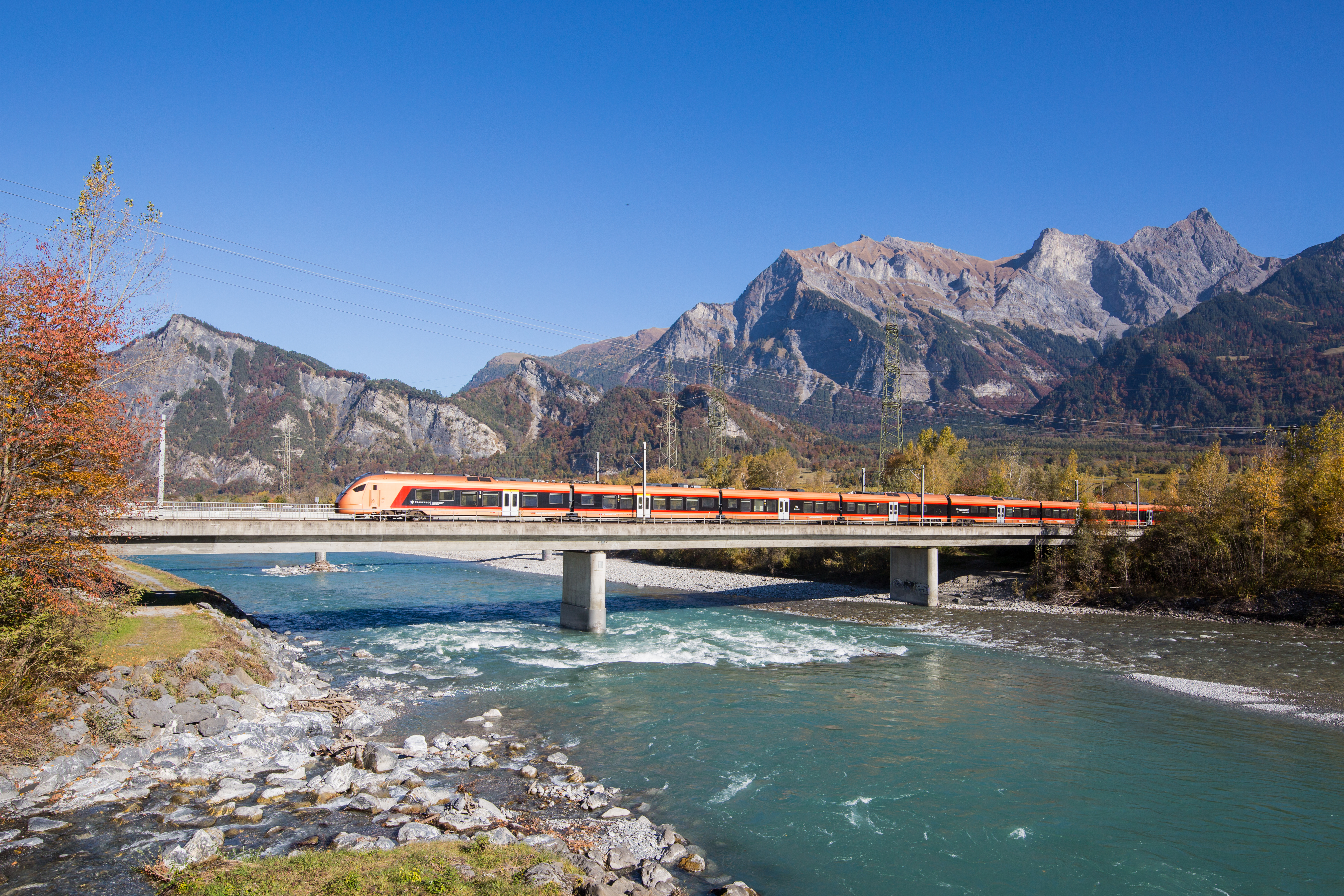 Kupferfarbener Zug fährt über eine Brücke vor Berglandschaft der Schweiz