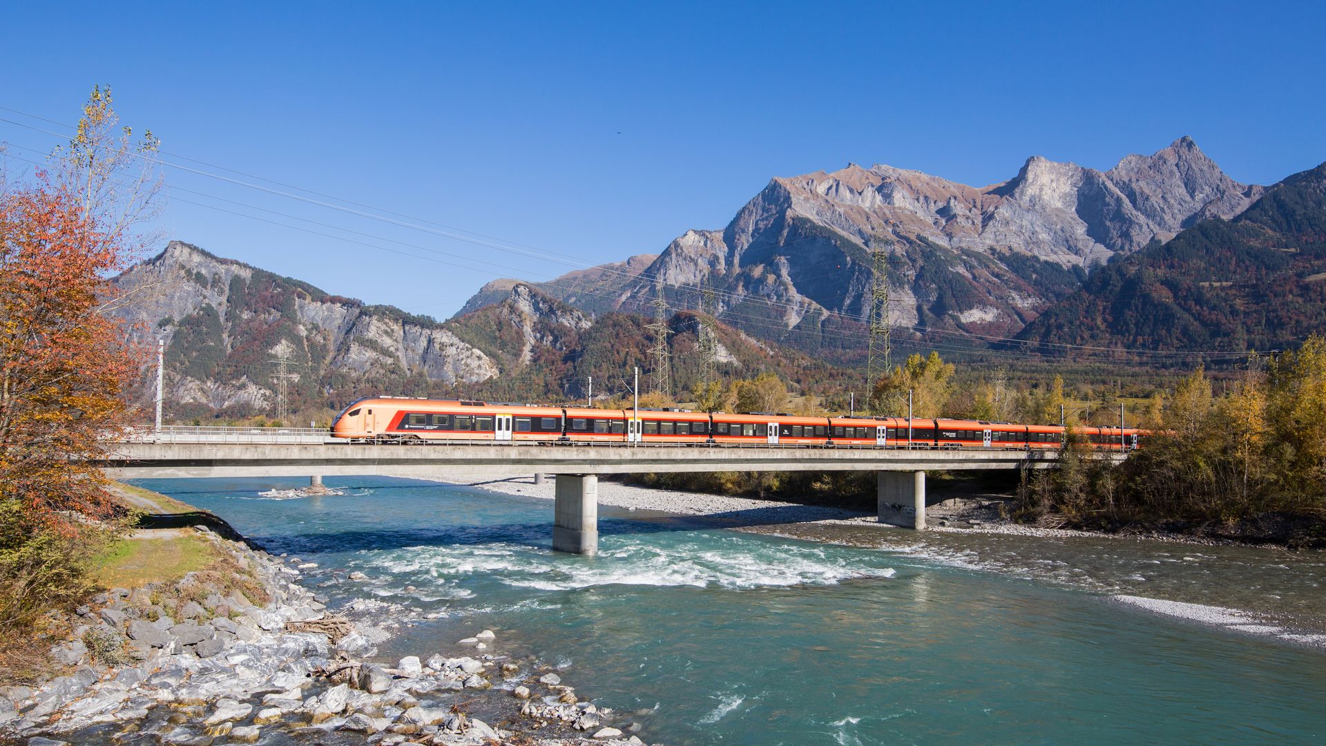 Kupferfarbener Zug fährt über eine Brücke vor Berglandschaft der Schweiz