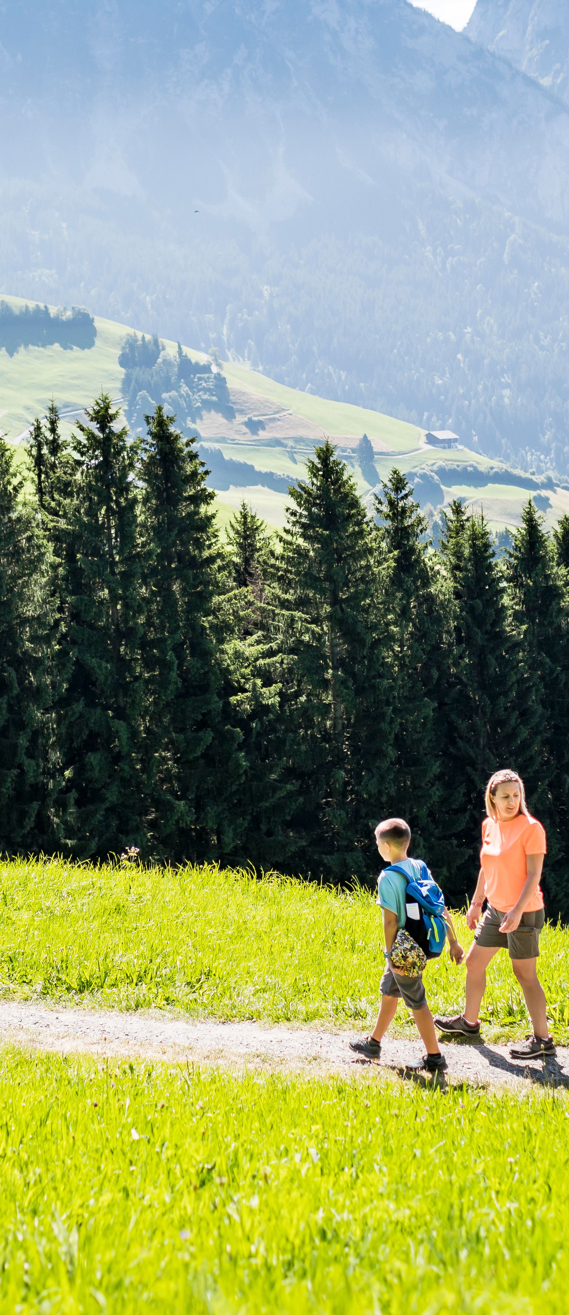 Family hiking along a sunny trail at Engelstock Sattel-Hochstuckli with views of lush forests, meadows, and the Swiss Pre-Alps.