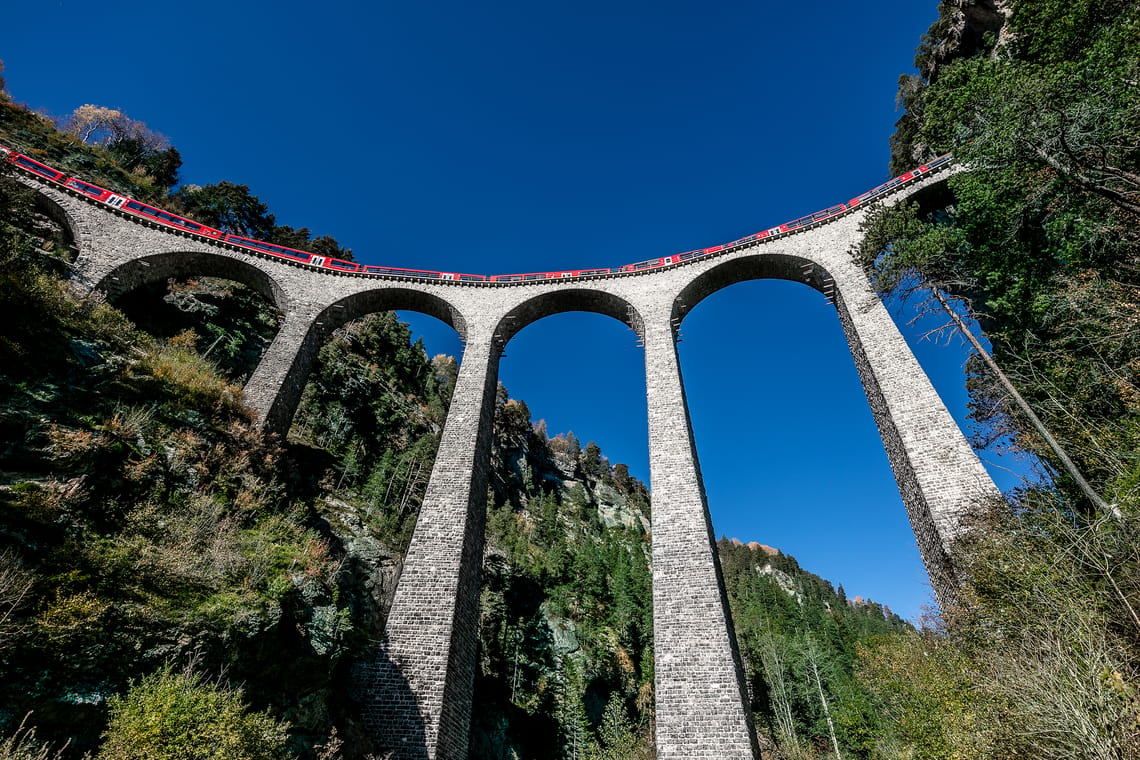 Roter Zug fährt über hohes Viadukt mit blauem Himmel