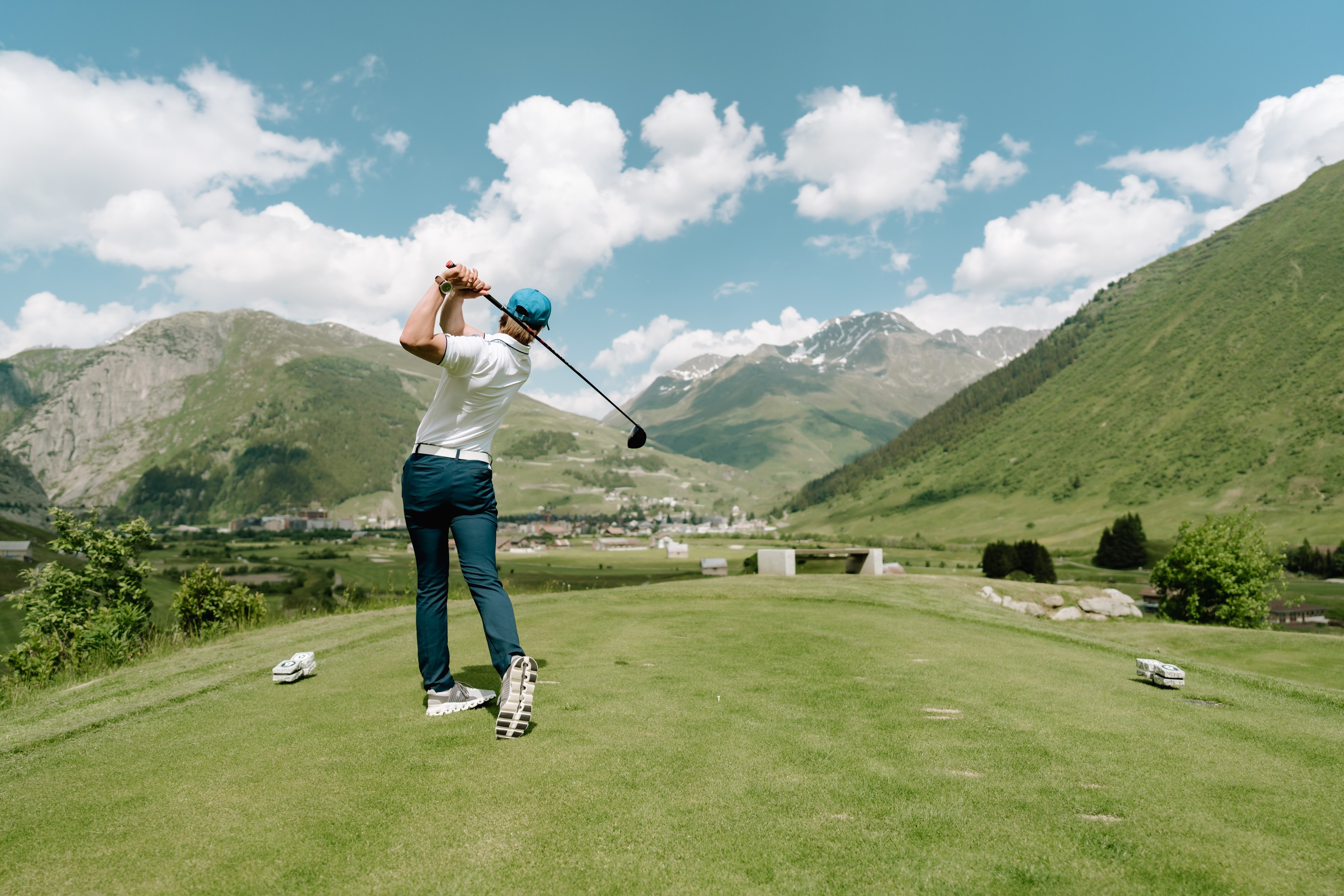 Golfer teeing off at Andermatt Golf Course, surrounded by green alpine valleys and snow-capped peaks – a unique sporting experience in central Switzerland.