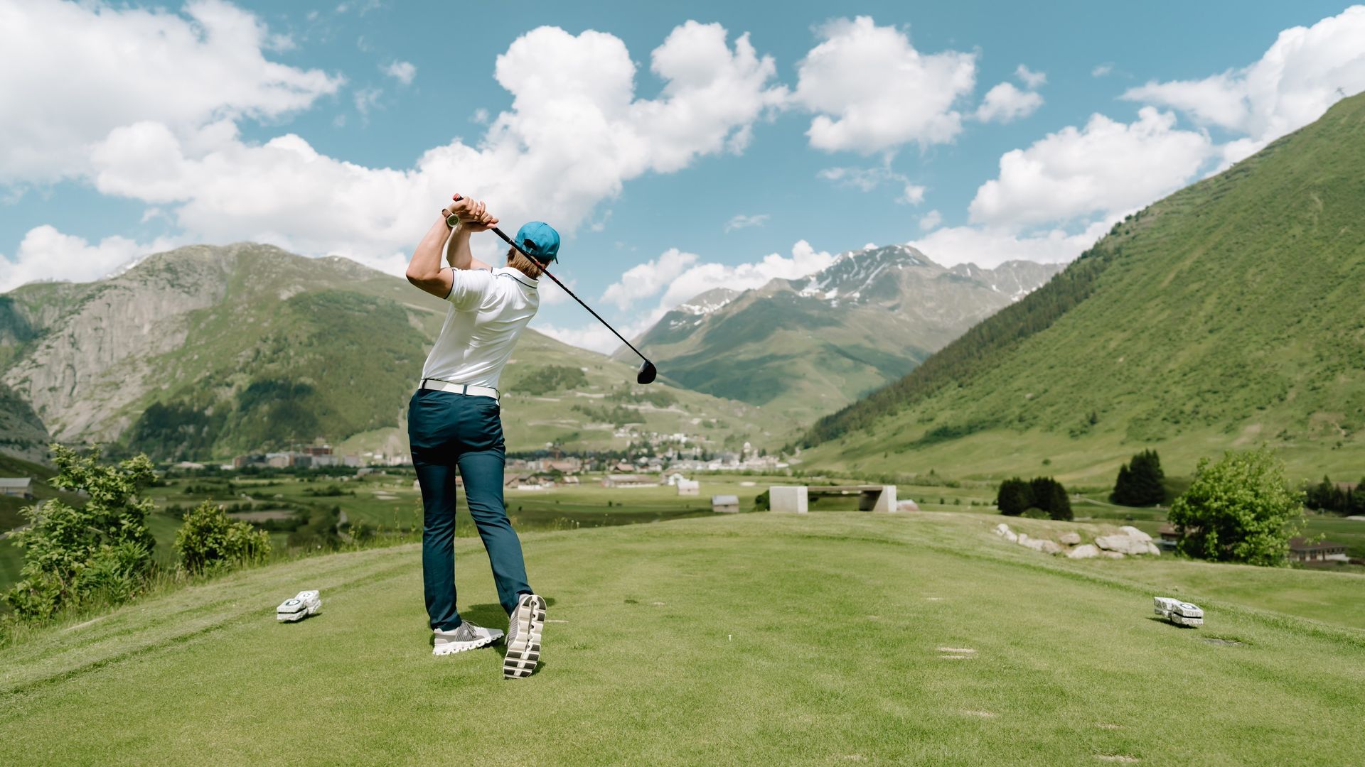 Golfer beim Abschlag auf dem Golfplatz Andermatt, umgeben von grünen Alpentälern und schneebedeckten Gipfeln – ein einzigartiges Sporterlebnis in der Zentralschweiz.