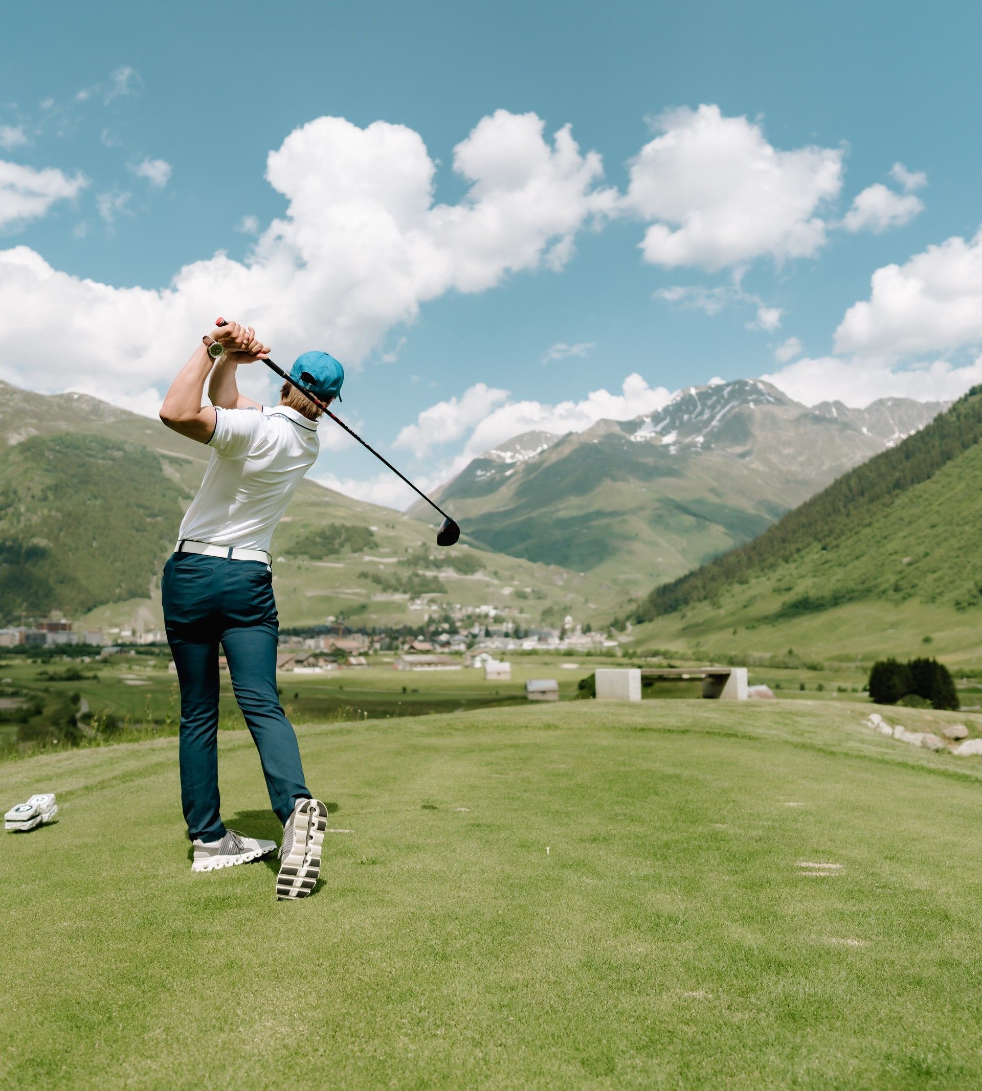 Golfeur au départ sur le terrain de golf d’Andermatt, entouré de vallées alpines verdoyantes et de sommets enneigés – une expérience sportive unique au cœur de la Suisse.
